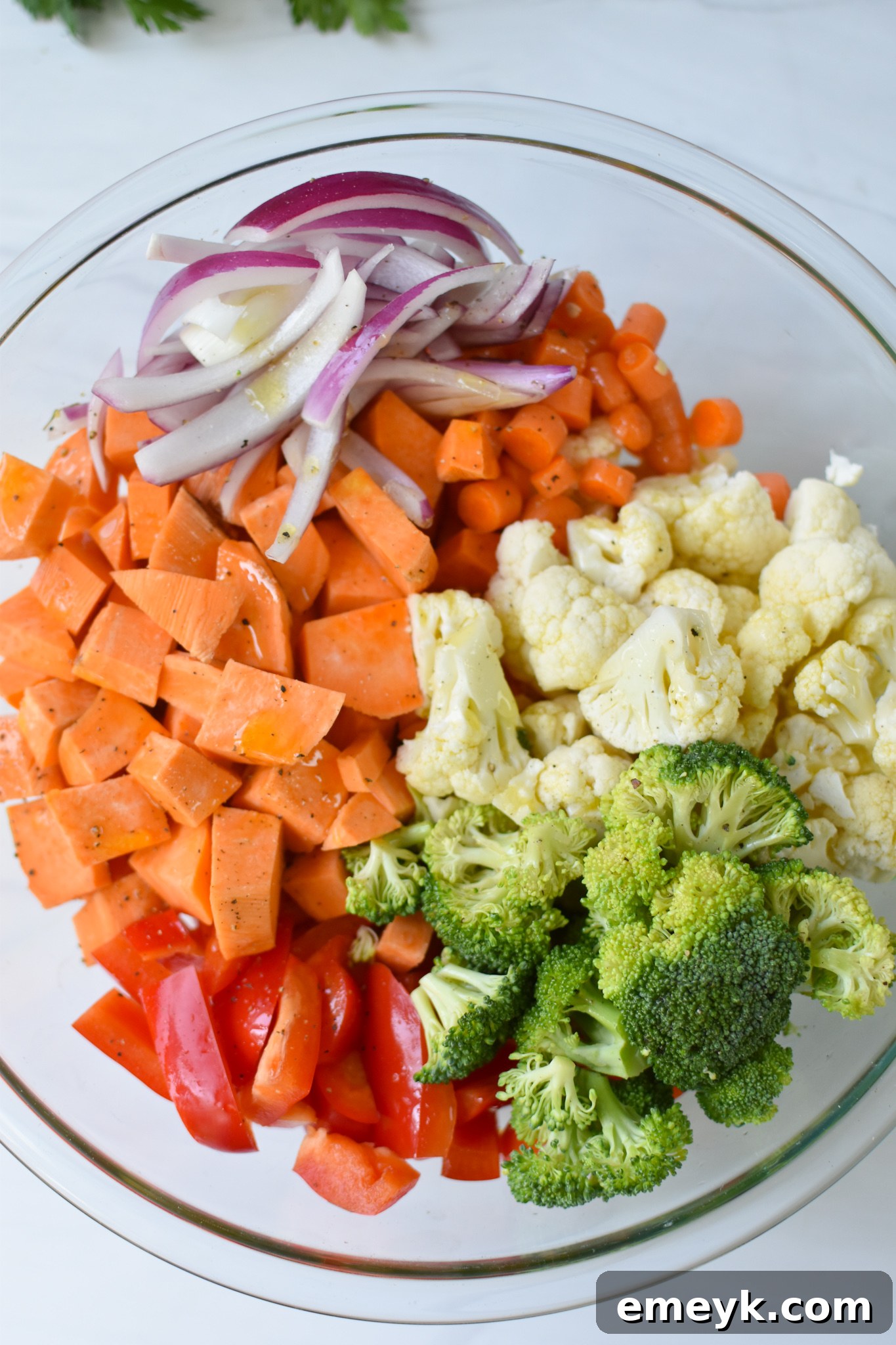 Mixed sweet potatoes and vegetables coated in olive oil and spices, ready for roasting on a baking sheet.
