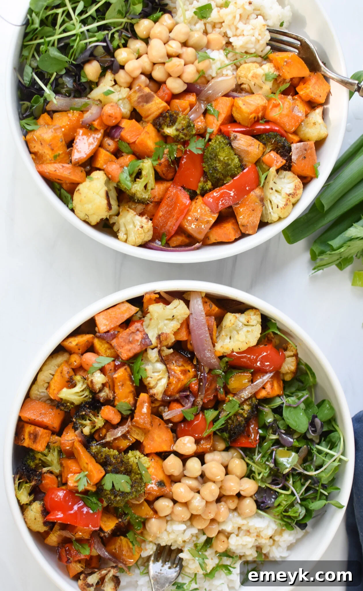 Two beautifully assembled Sweet Potato Bowls with roasted vegetables, grains, chickpeas, and fresh herbs, drizzled with tahini dressing.