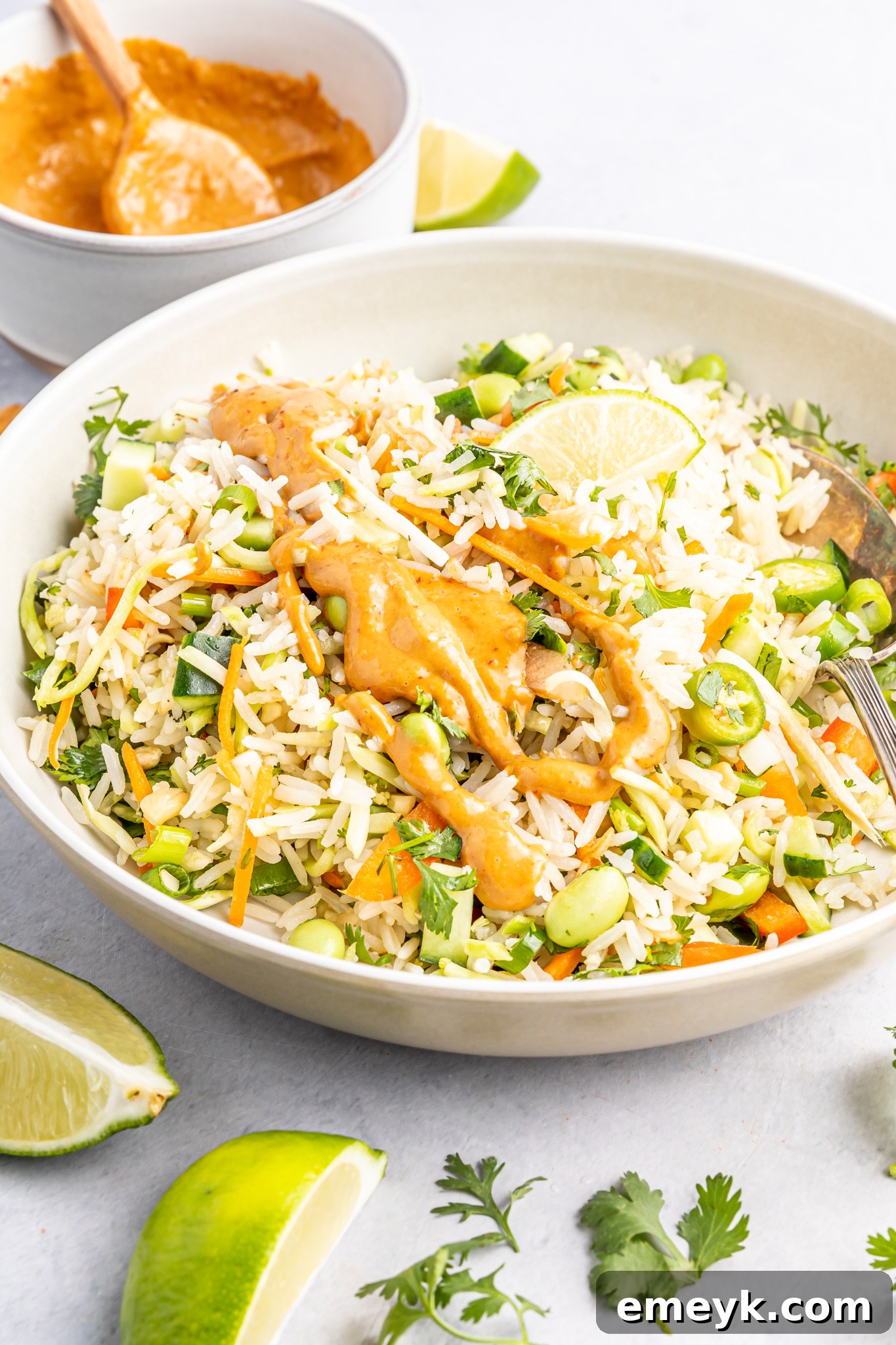 Coconut Rice Salad being tossed with the rich peanut dressing in a large bowl, ready to be served.