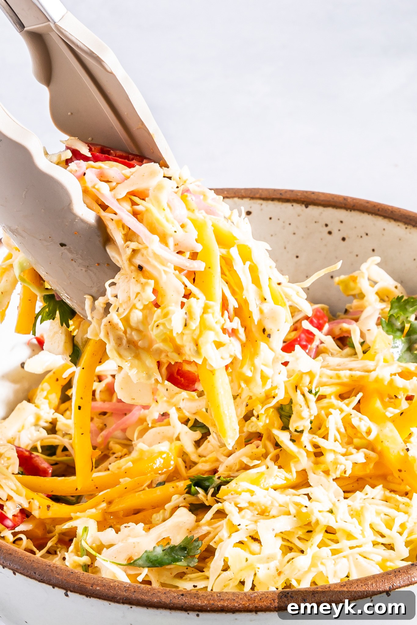 A close-up shot of Easy Caribbean Coleslaw being tossed with tongs in a large bowl, ready to serve.