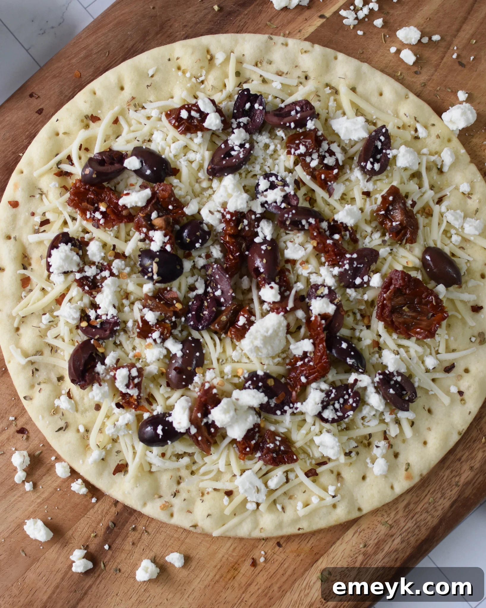 Hellenic Pizza 5 Greek Pizza base with mozzarella, olives, and sun-dried tomatoes before baking.