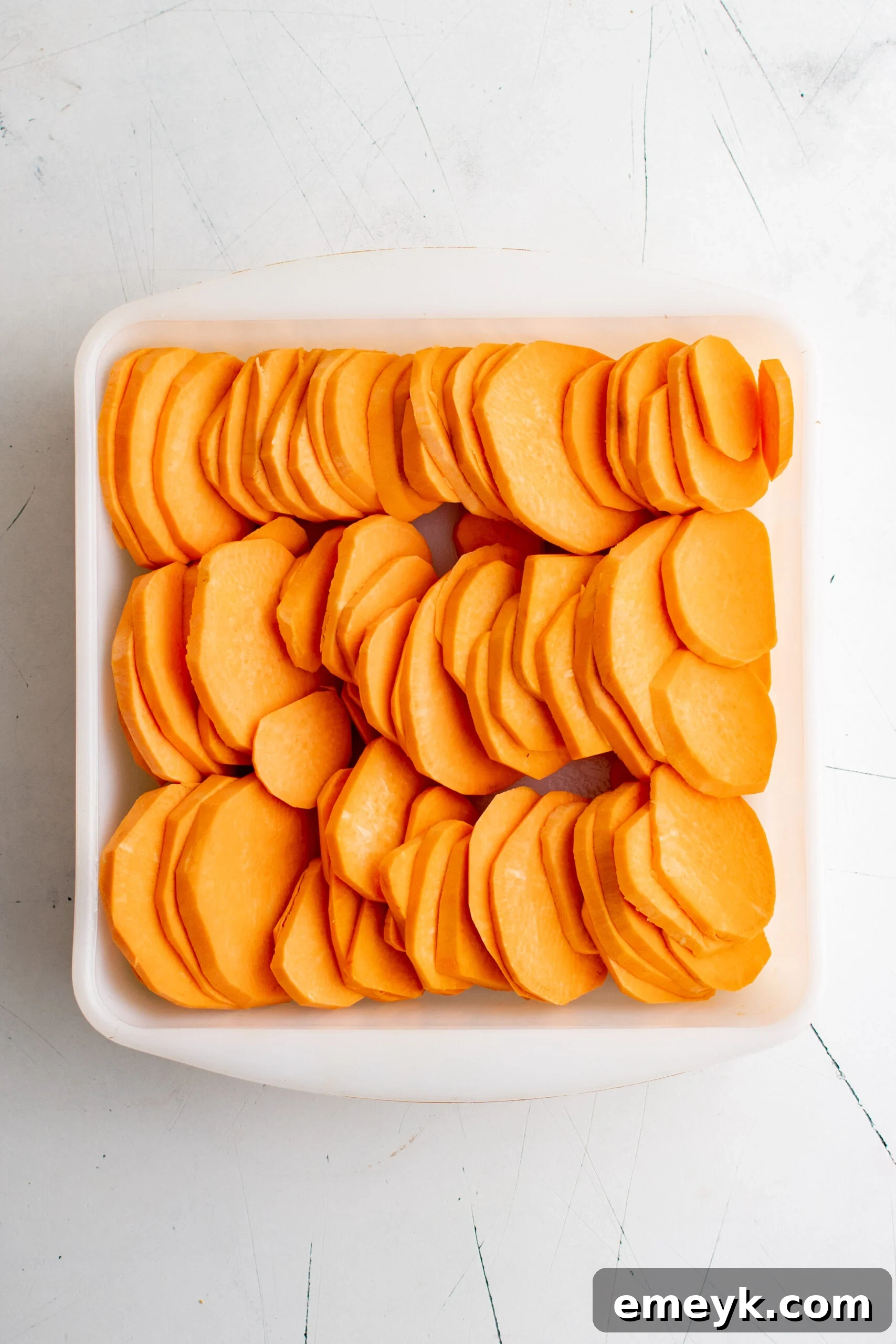 Easy Scalloped Sweet Potatoes with sliced sweet potatoes arranged in a dish with cream.