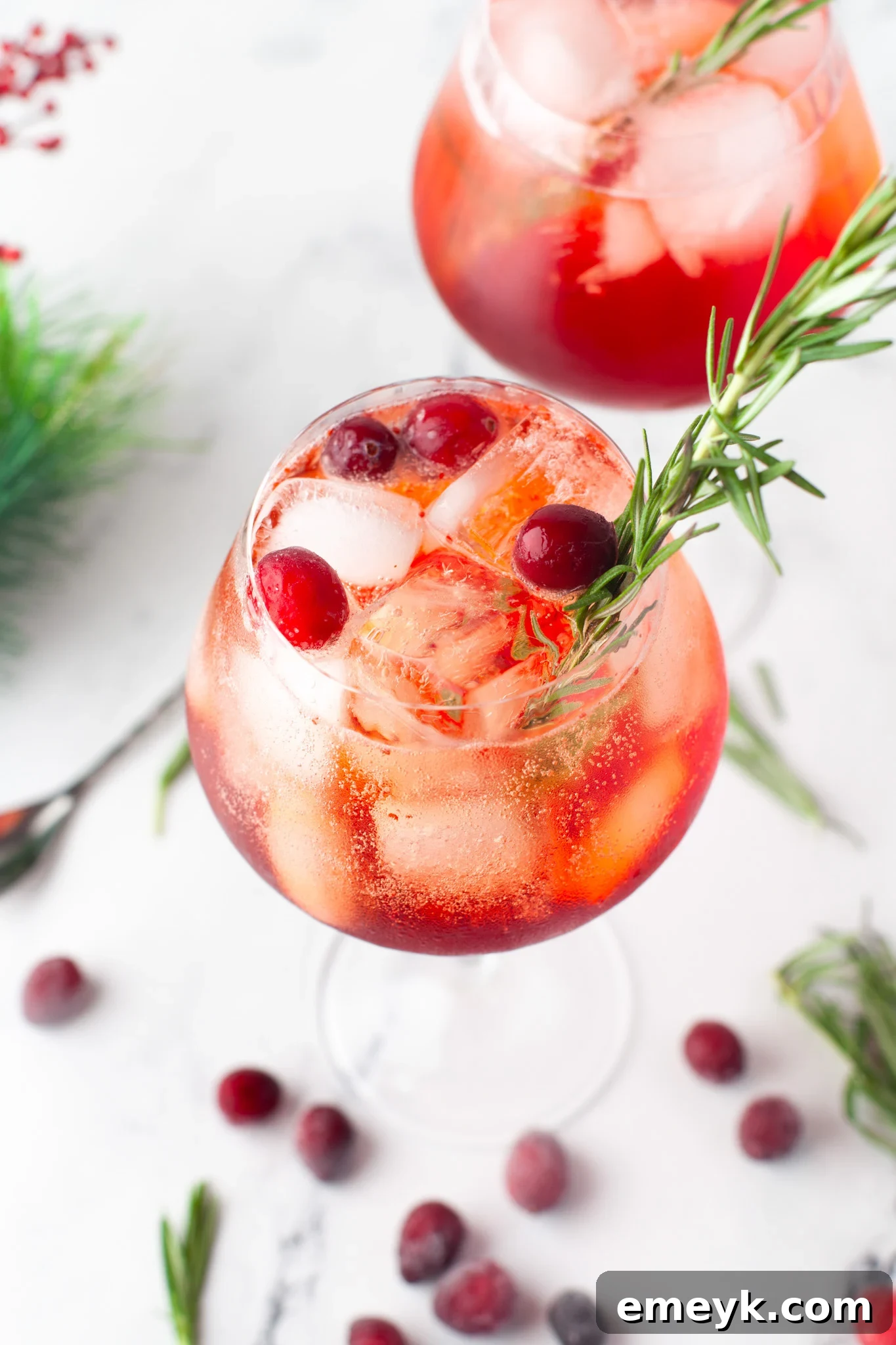 Two Cranberry Aperol Spritz cocktails in elegant glasses, garnished with fresh cranberries and rosemary, set against a festive background.
