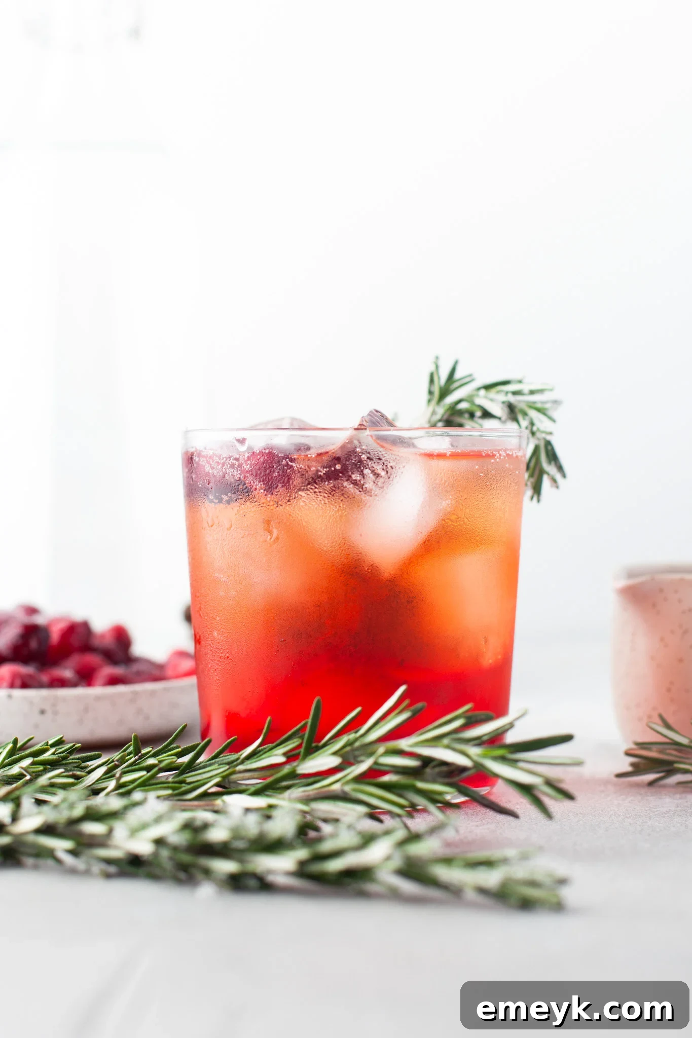 A single Cranberry Aperol Spritz cocktail in a modern short glass, elegantly garnished with rosemary and fresh cranberries, ready to be served.