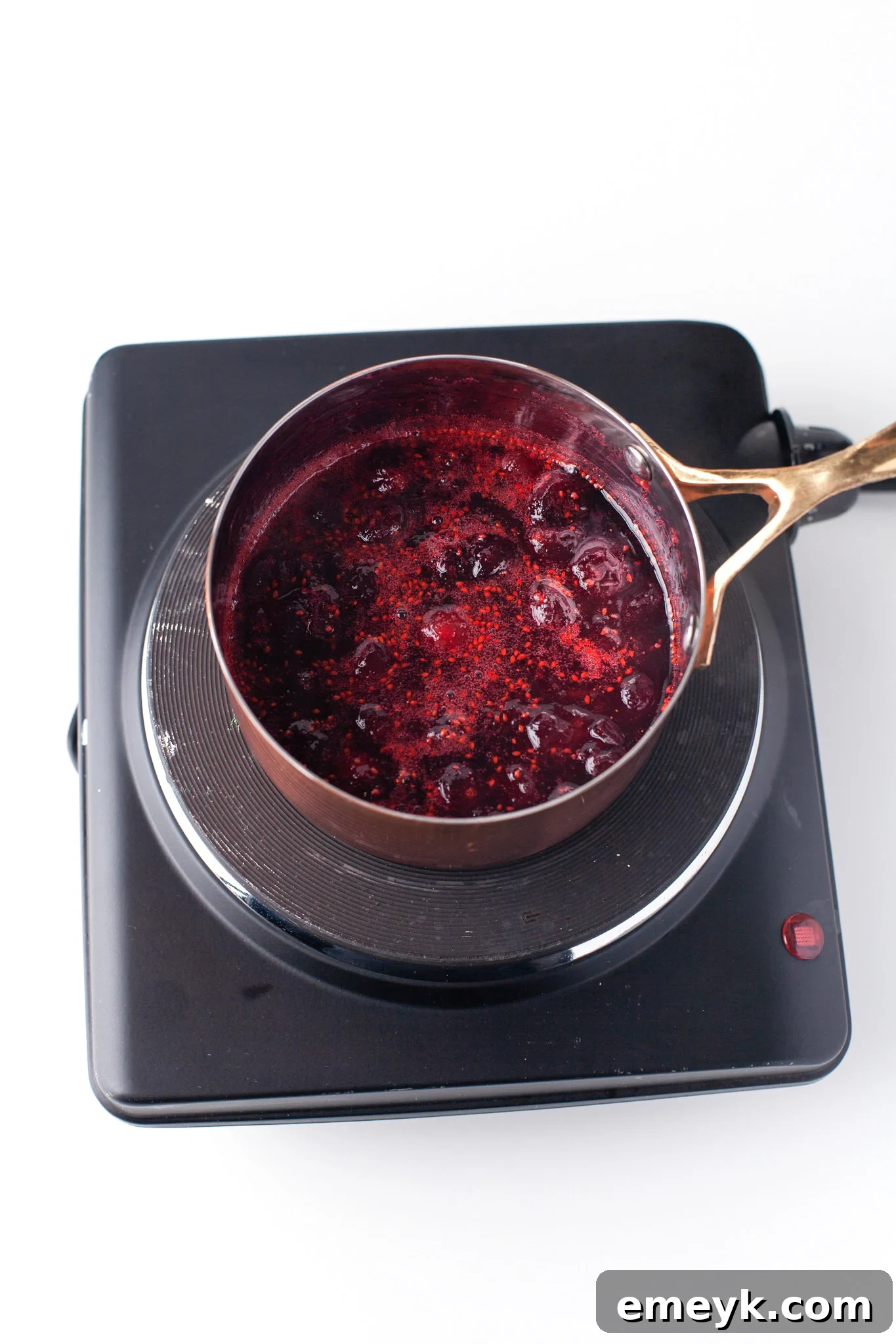 Fresh cranberries, granulated sugar, and water simmering in a small saucepan on a stovetop, capturing the initial stage of homemade cranberry syrup preparation.