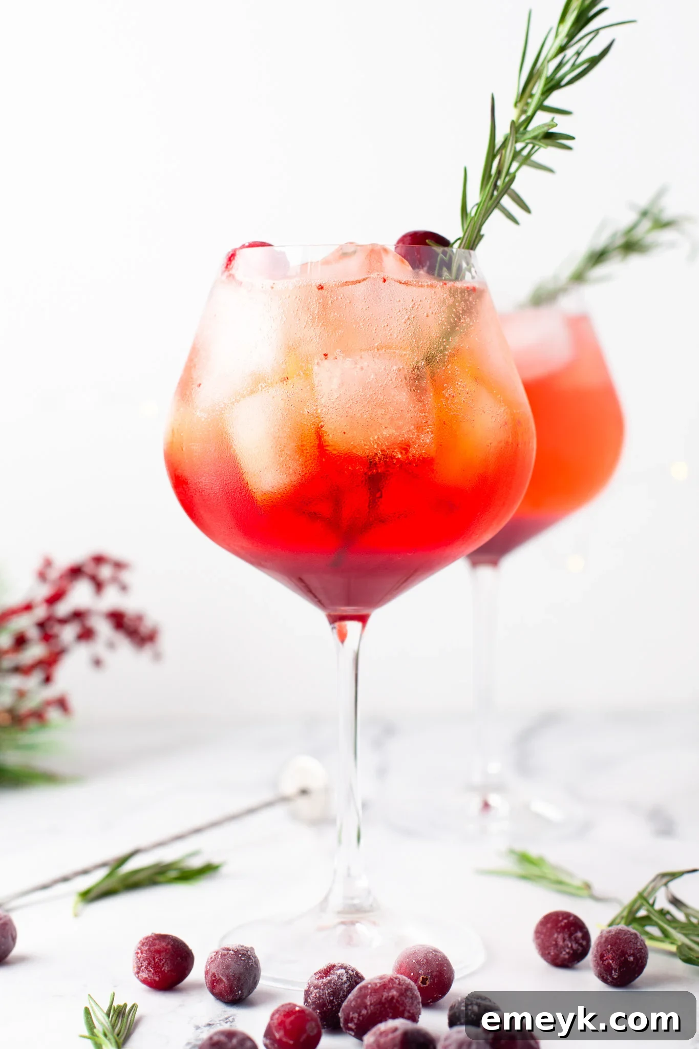 A close-up of a Cranberry Aperol Spritz garnished with fresh rosemary and cranberries, highlighting the festive appeal of the cocktail.