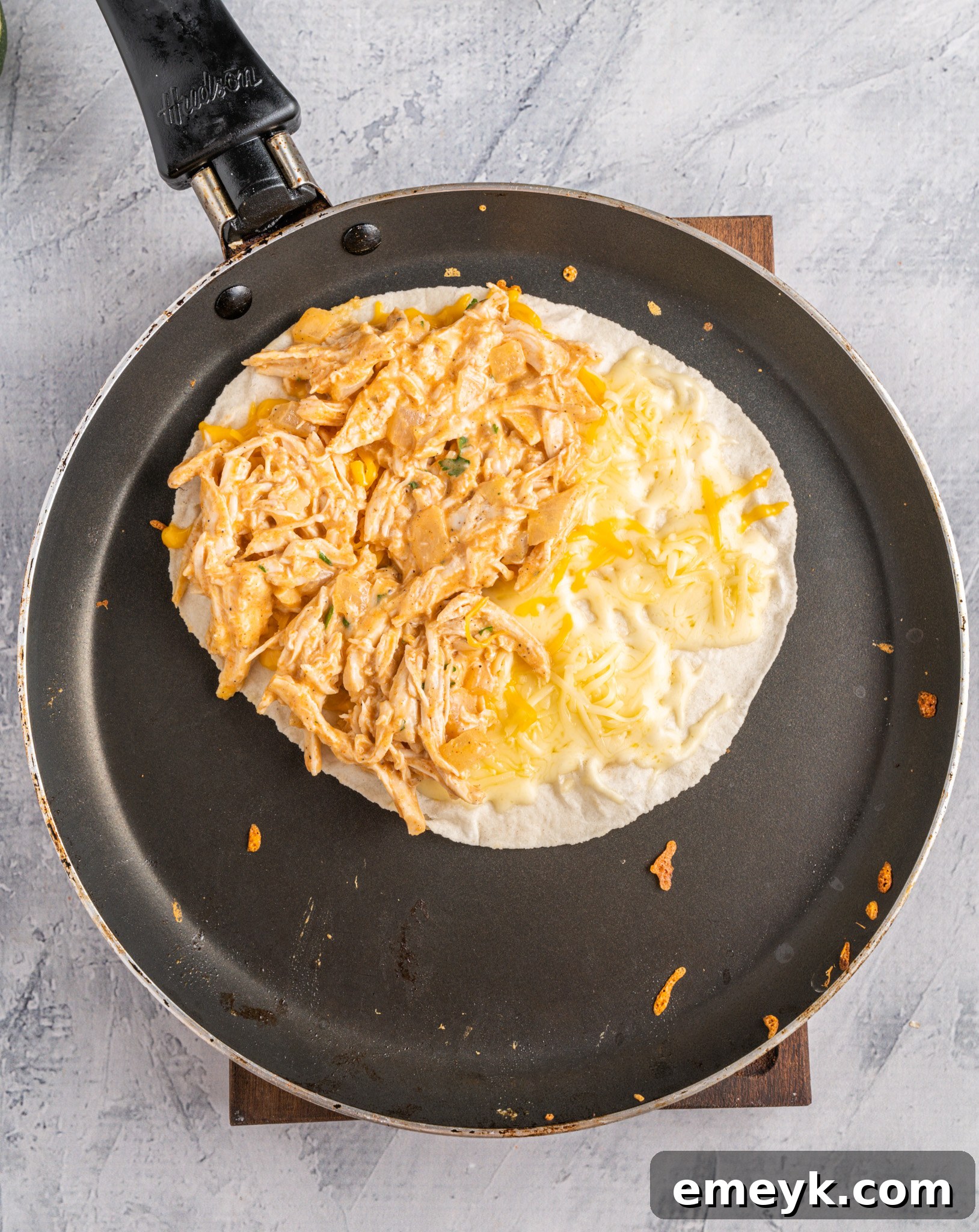Quick Buffalo Chicken Quesadilla 8 Tortilla in a skillet with cheese and buffalo chicken filling on one half, ready to be folded