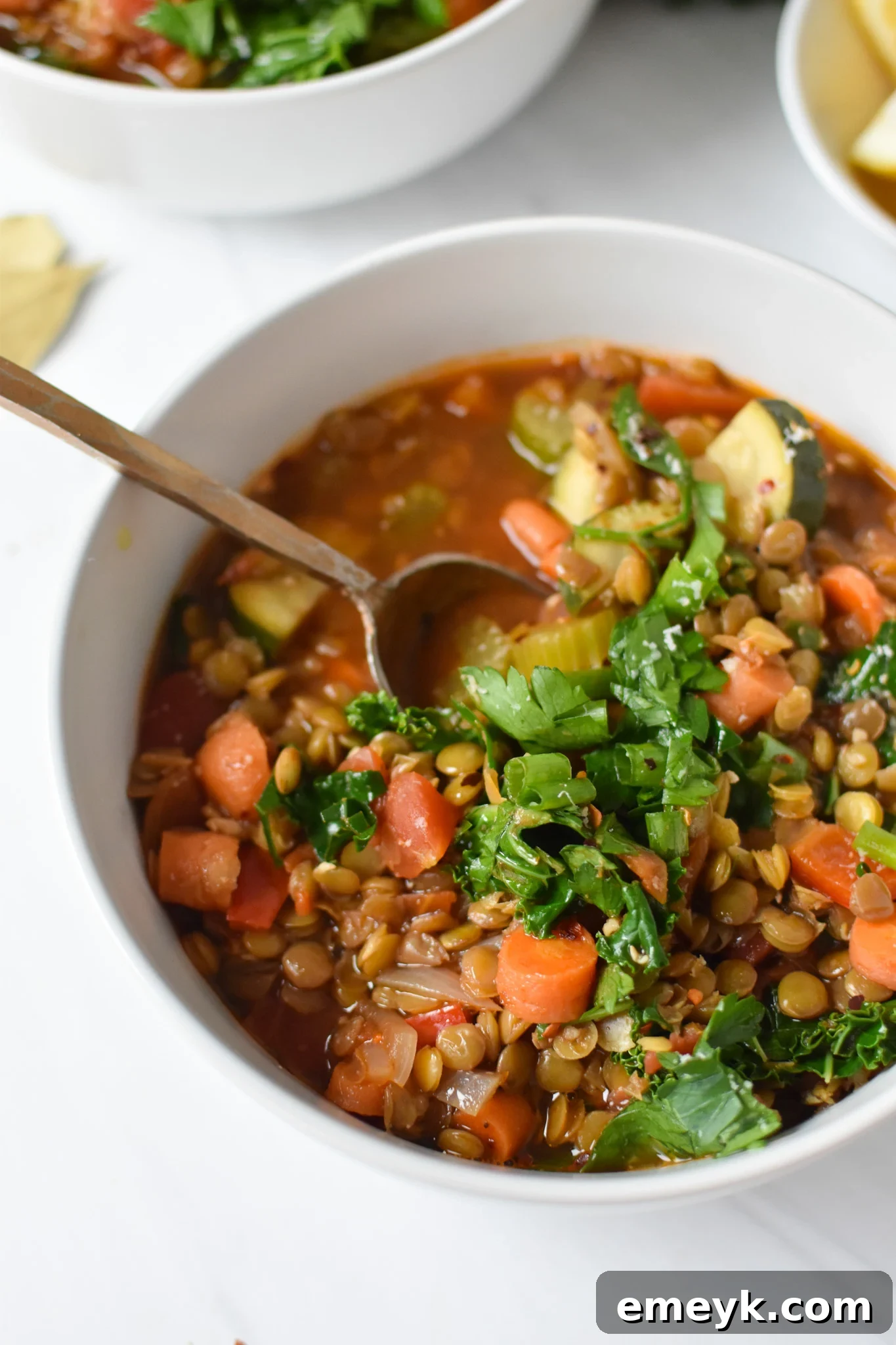 A bowl of Italian Style Lentil Soup with a gold spoon, garnished with fresh parsley and red pepper flakes.