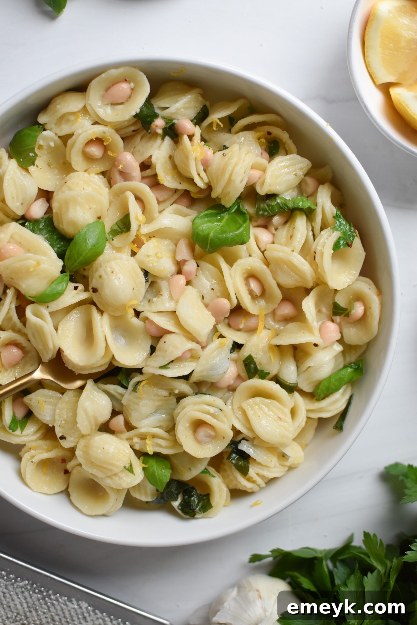 Zesty Lemon Basil White Bean Pasta 2 A serving of Lemon Basil White Bean Pasta in a white bowl, garnished with fresh basil leaves and a lemon wedge.