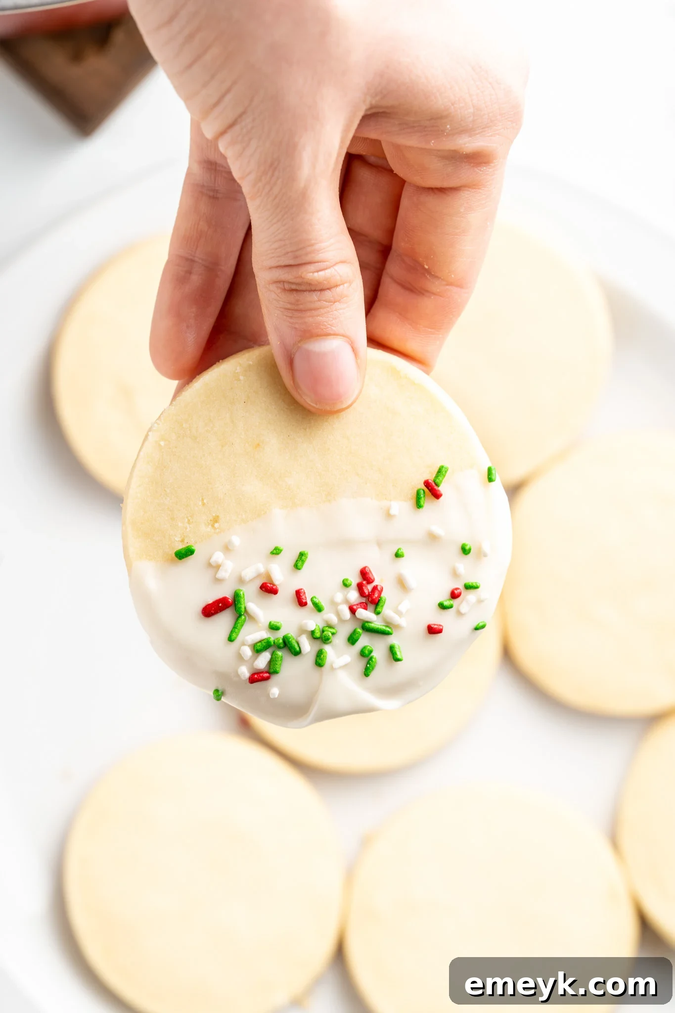 Christmas Shortbread Cookie being decorated with melted white chocolate and sprinkles.