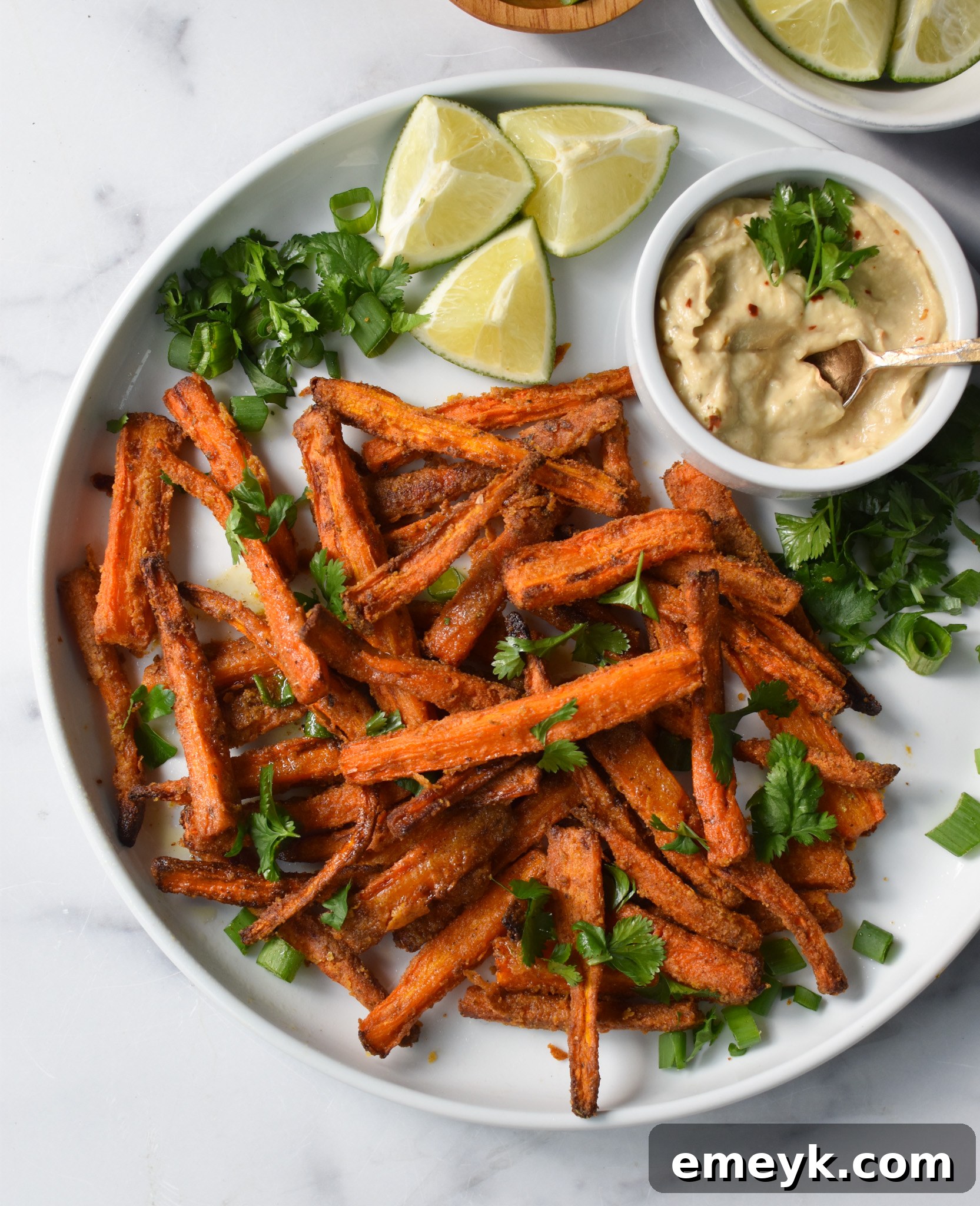 Golden Roasted Carrot Fries 6 Close-up of golden and crispy Oven Baked Carrot Fries on a white round plate, garnished with fresh herbs.