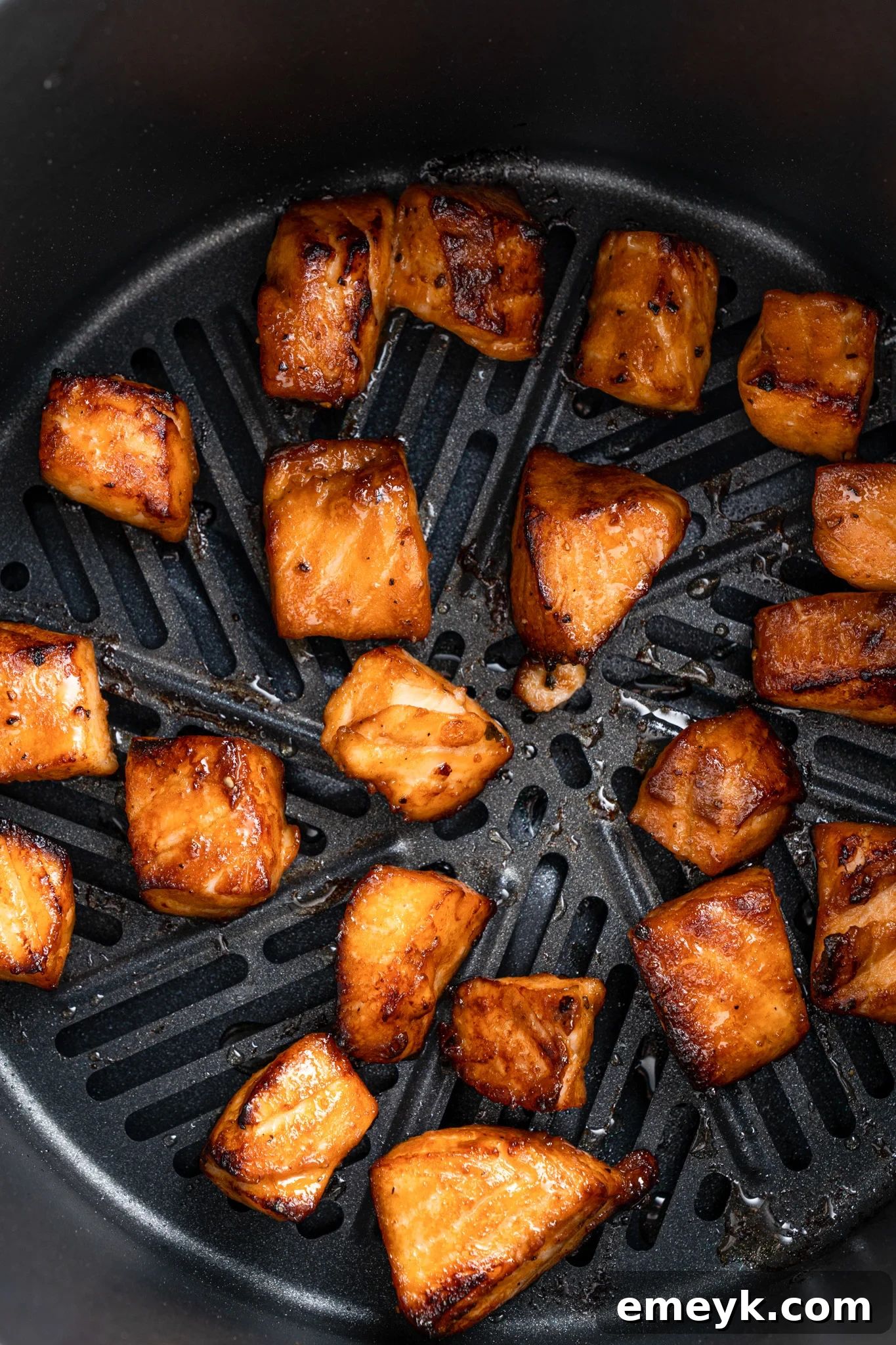 Chunks of glazed salmon are evenly spaced and cooked inside an air fryer basket. The pieces are golden brown with a slight char, indicating they are cooked and ready to eat.