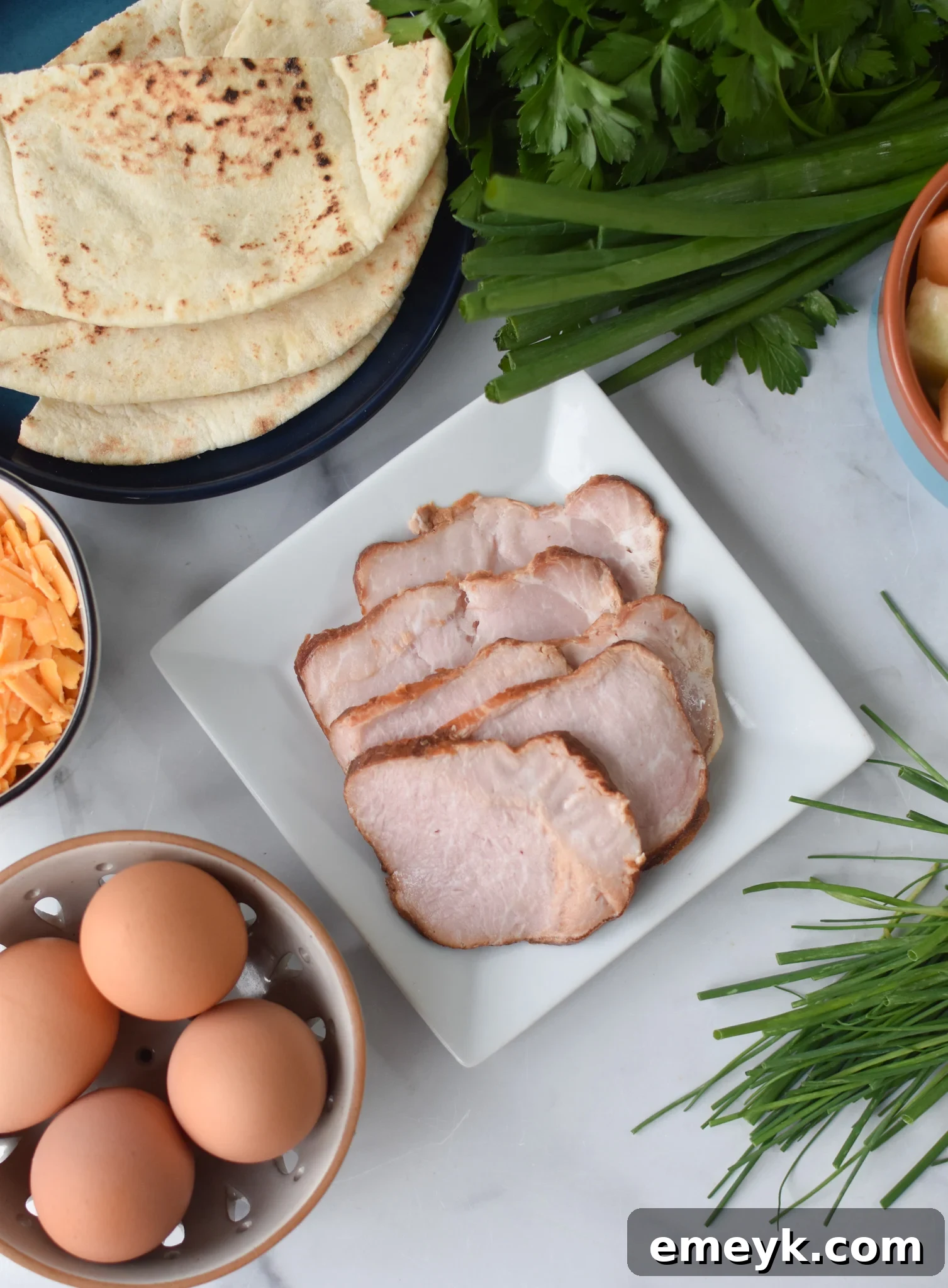 Sunrise Pita Pockets 3 Fresh ingredients laid out for the Breakfast Pita Recipe, including eggs, bacon, pita bread, cheese, and chives.