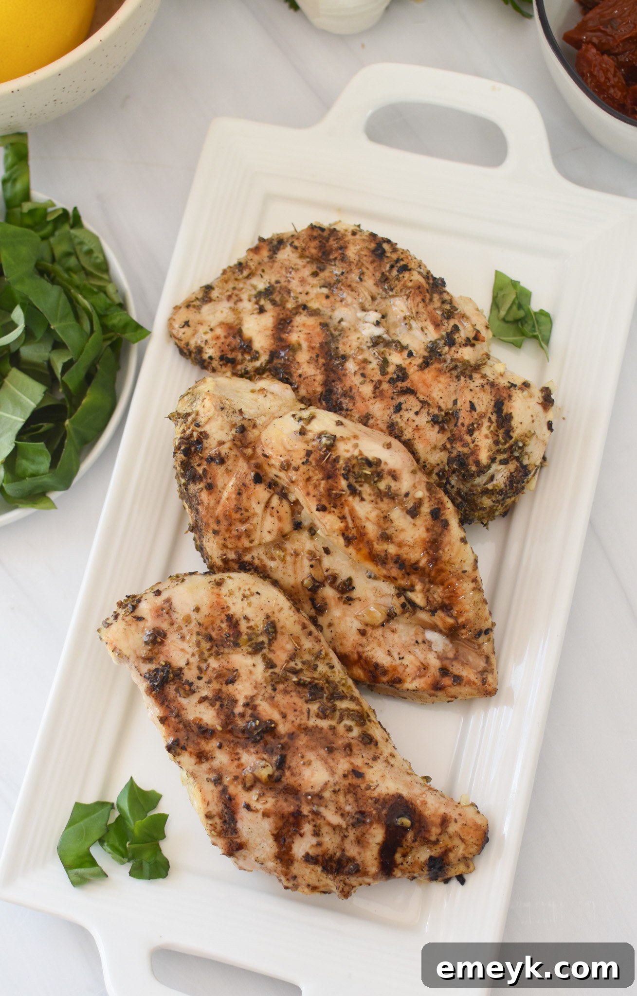 Grilled chicken breasts resting on a white plate, ready for the Chicken Bryan toppings.