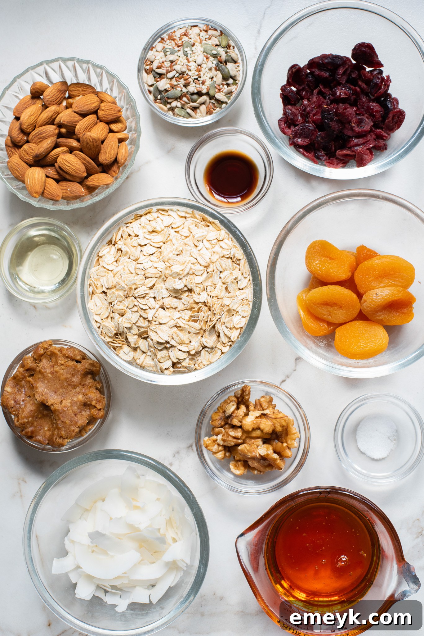 A colorful array of ingredients for easy date granola bars, including dates, oats, dried apricots, cranberries, and various nuts and seeds, laid out on a clean white surface.