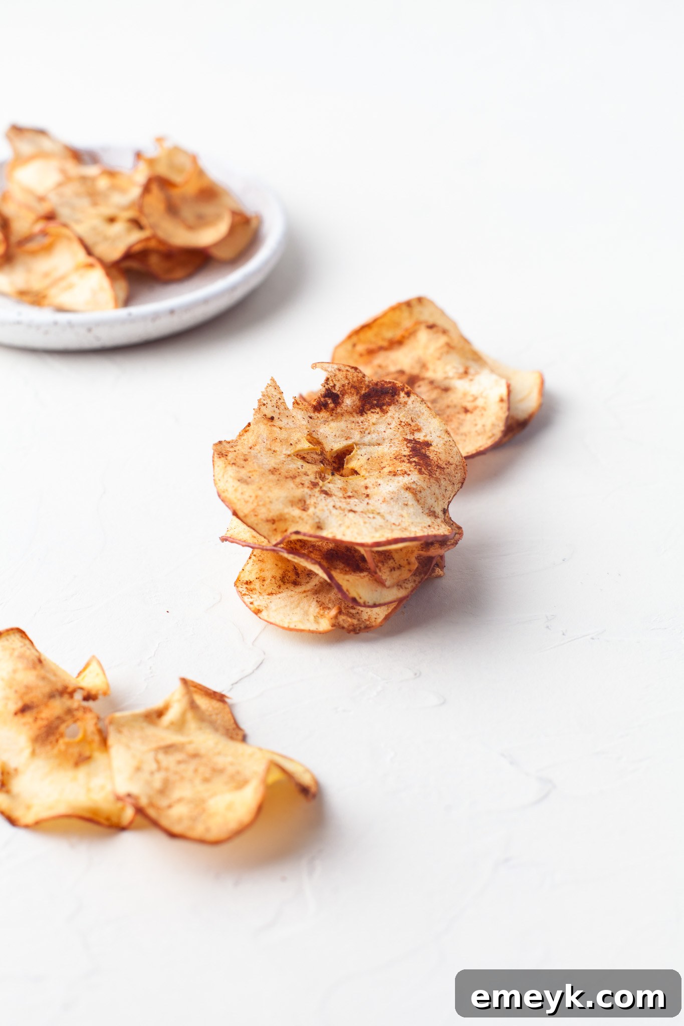 Crispy Air Fryer Apple Chips 9 A bowl of delicious Air Fryer Apple Chips on a white table, ready to be eaten.