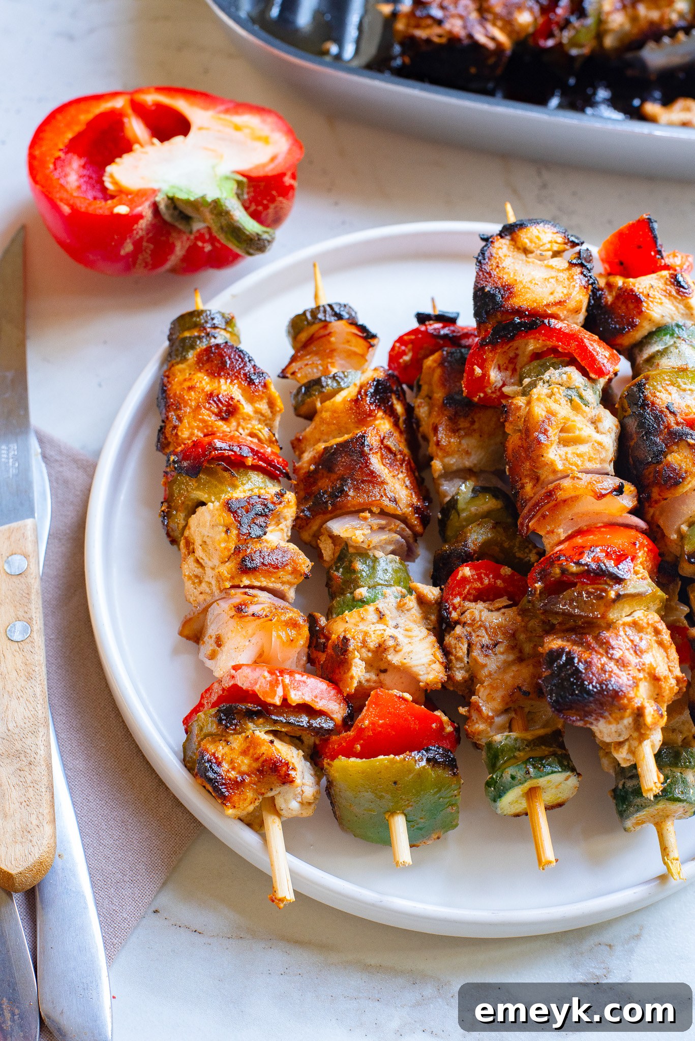 Lemon-Herb Mediterranean Chicken Skewers 2 Greek Marinated Chicken Kabobs with Lemon on a white plate, garnished with fresh herbs.