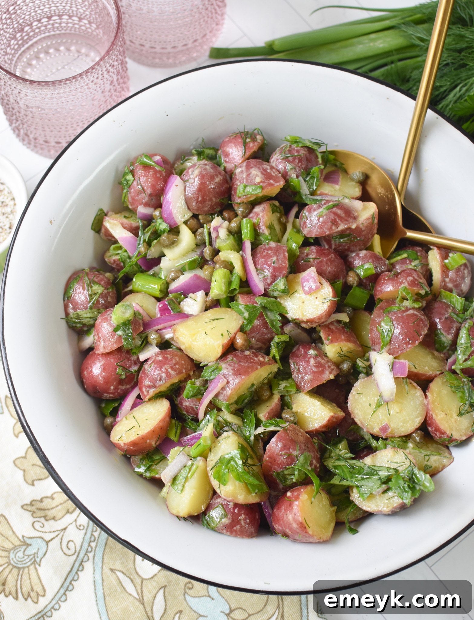 Bright & Zesty Potato Salad 2 A beautifully presented No Mayo Potato Salad in a white bowl, garnished with fresh herbs, with gold serving spoons beside it, inviting you to taste this light and zesty summer side dish.
