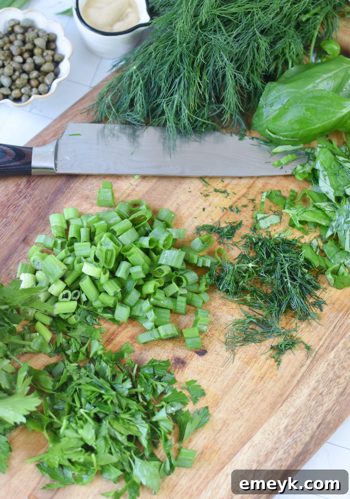 Bright & Zesty Potato Salad 10 A cutting board laden with a vibrant medley of fresh herbs—parsley, basil, and dill—finely minced and ready to be incorporated into the No Mayo Potato Salad.