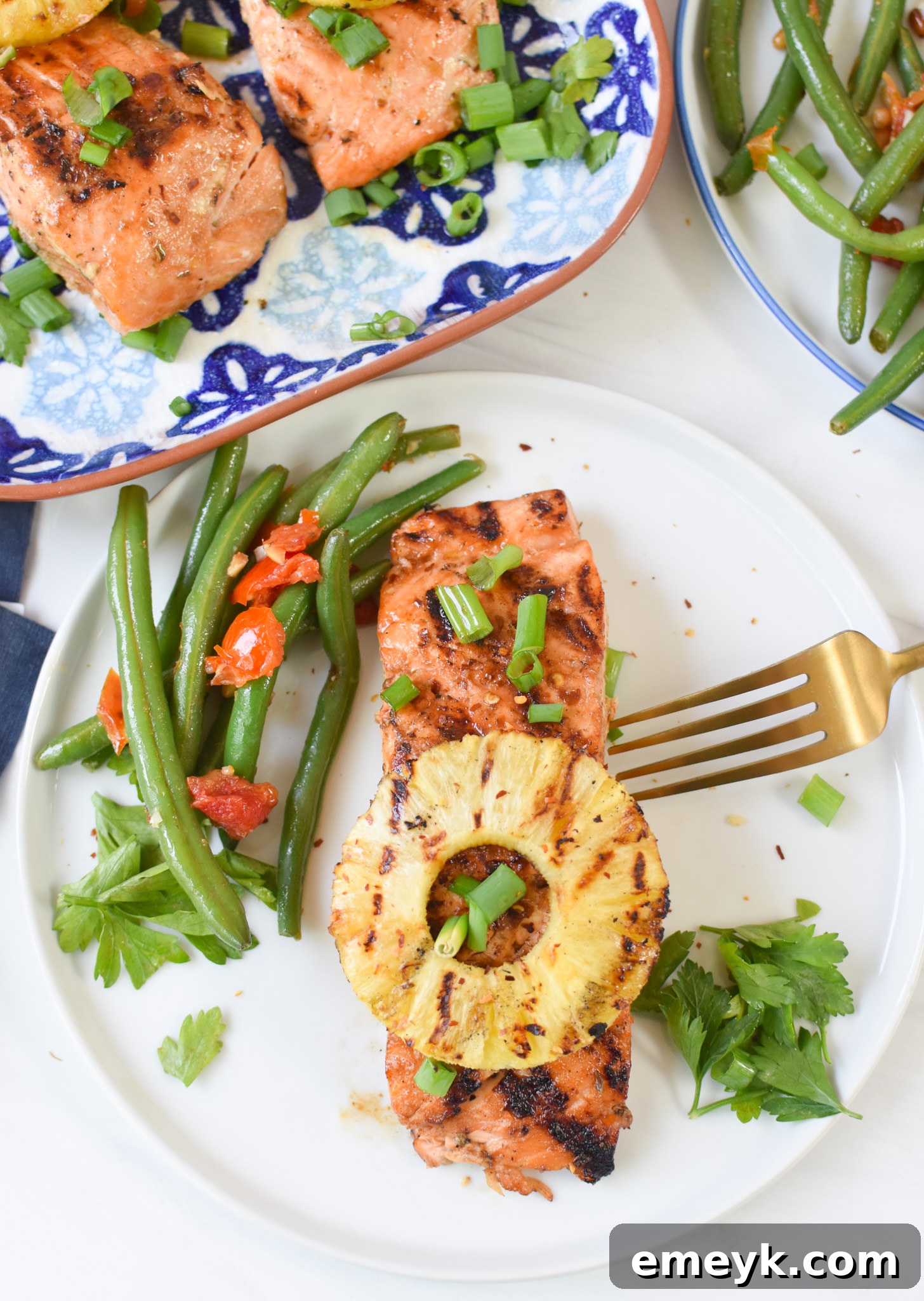Two pieces of Hawaiian Grilled Salmon on a white plate, served with grilled pineapple rings and garnished with vibrant green onions.