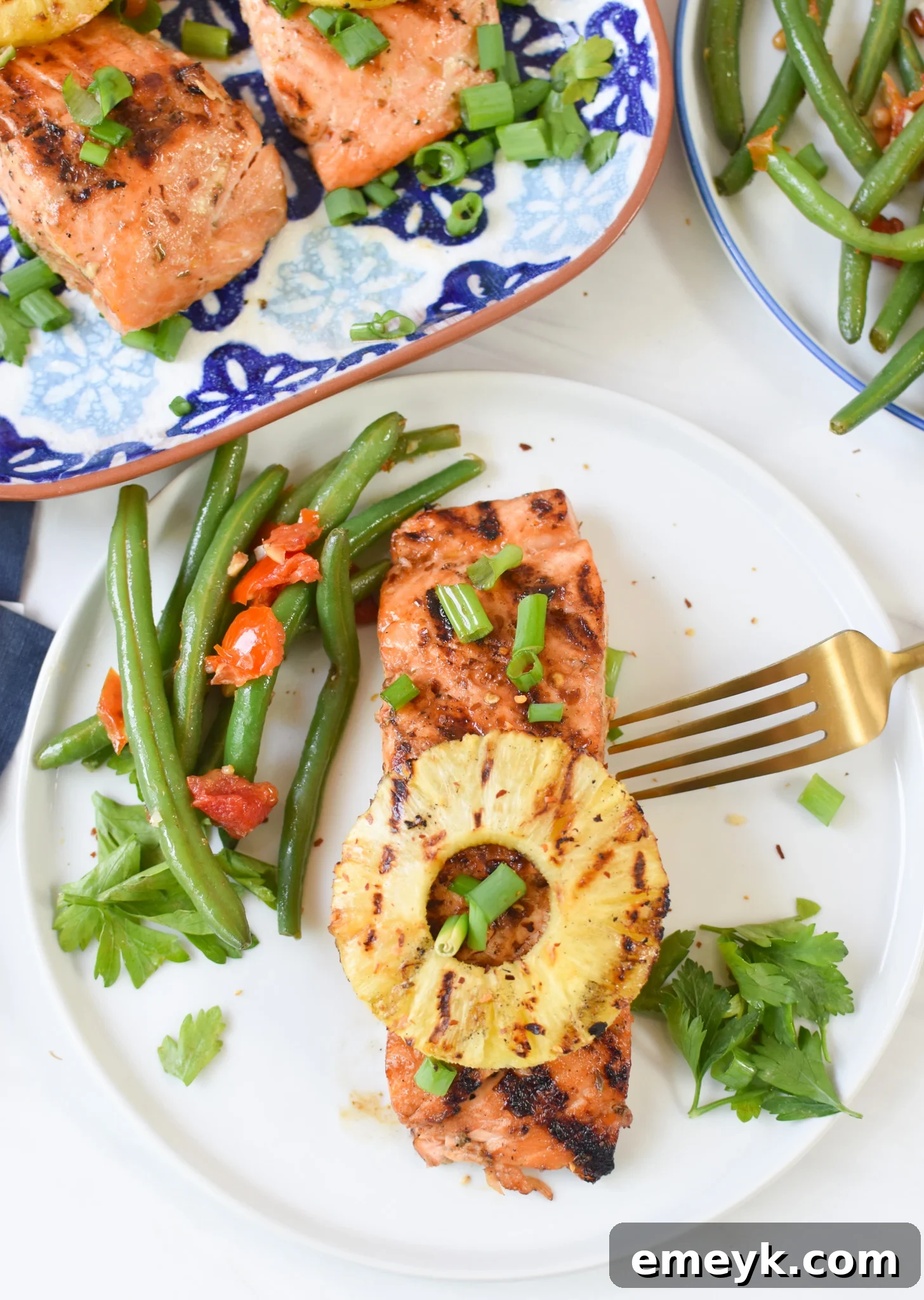 A serving of Hawaiian Grilled Salmon with perfectly cooked green beans and a slice of grilled pineapple on a white plate, elegantly garnished with fresh herbs.