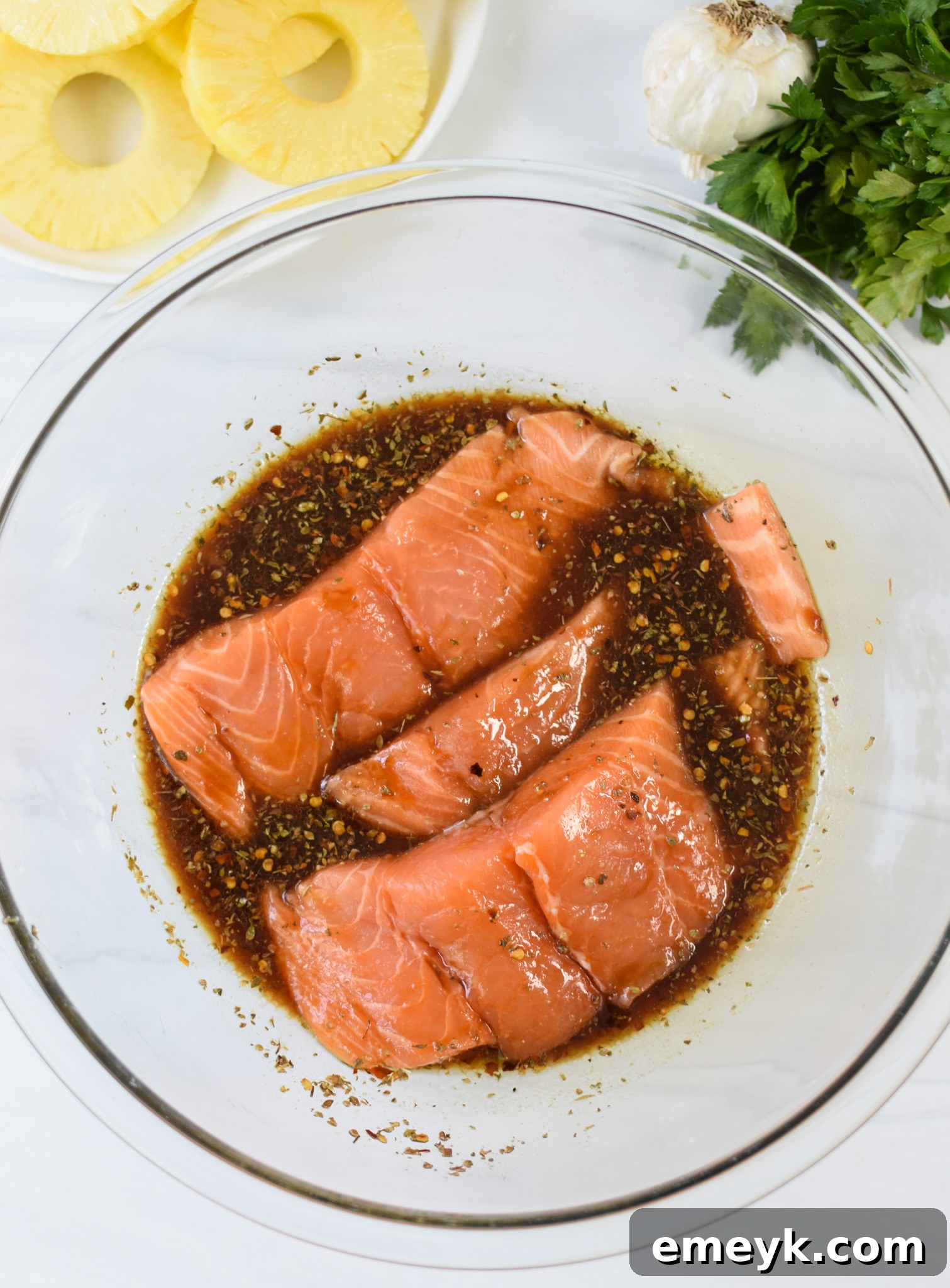Hawaiian Grilled Salmon fillets marinating in a bowl, fully coated in the tropical sauce.