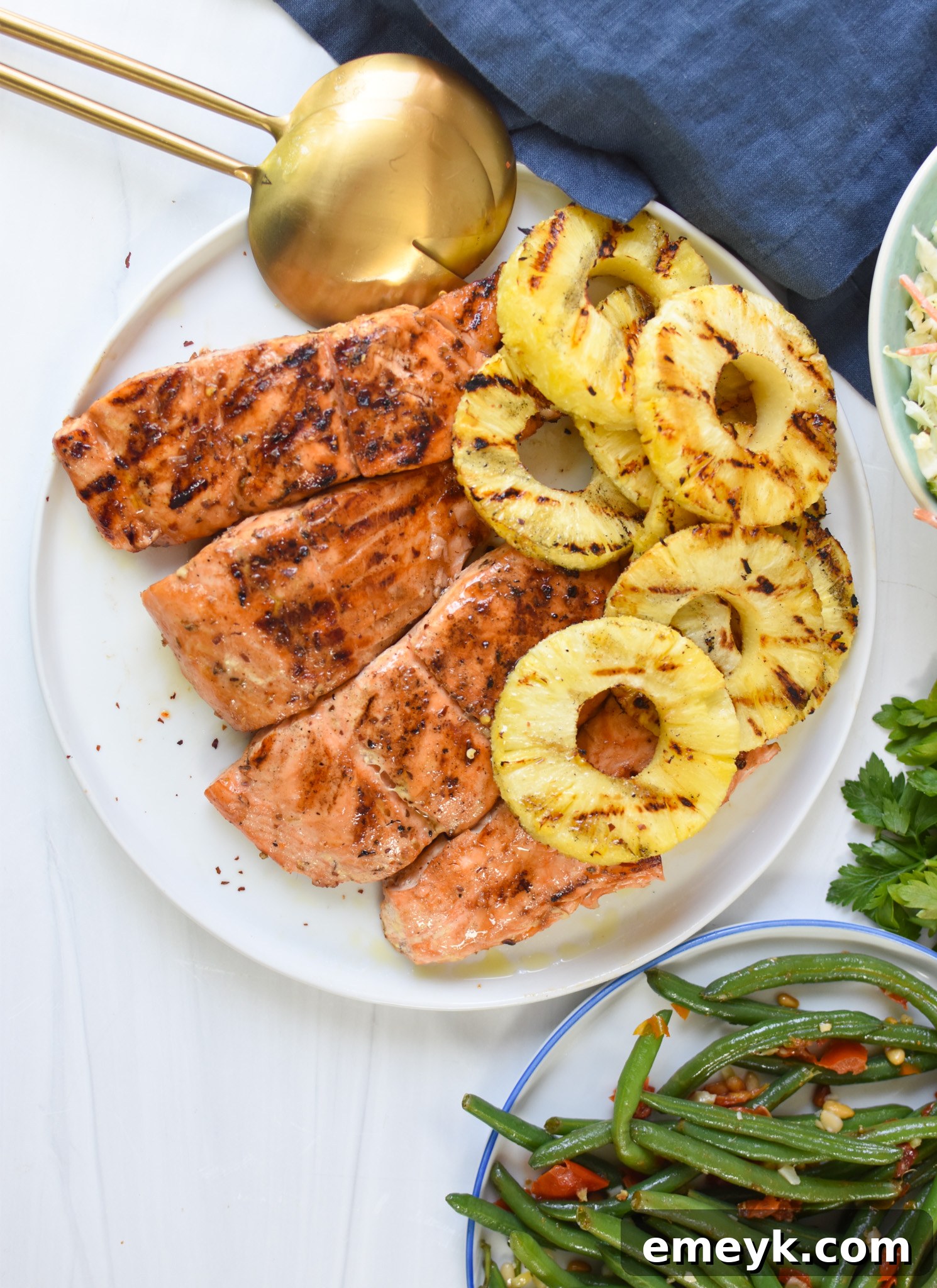 Hawaiian Grilled Salmon served with fresh green beans on a white plate, beautifully garnished with herbs and a side of grilled pineapple.