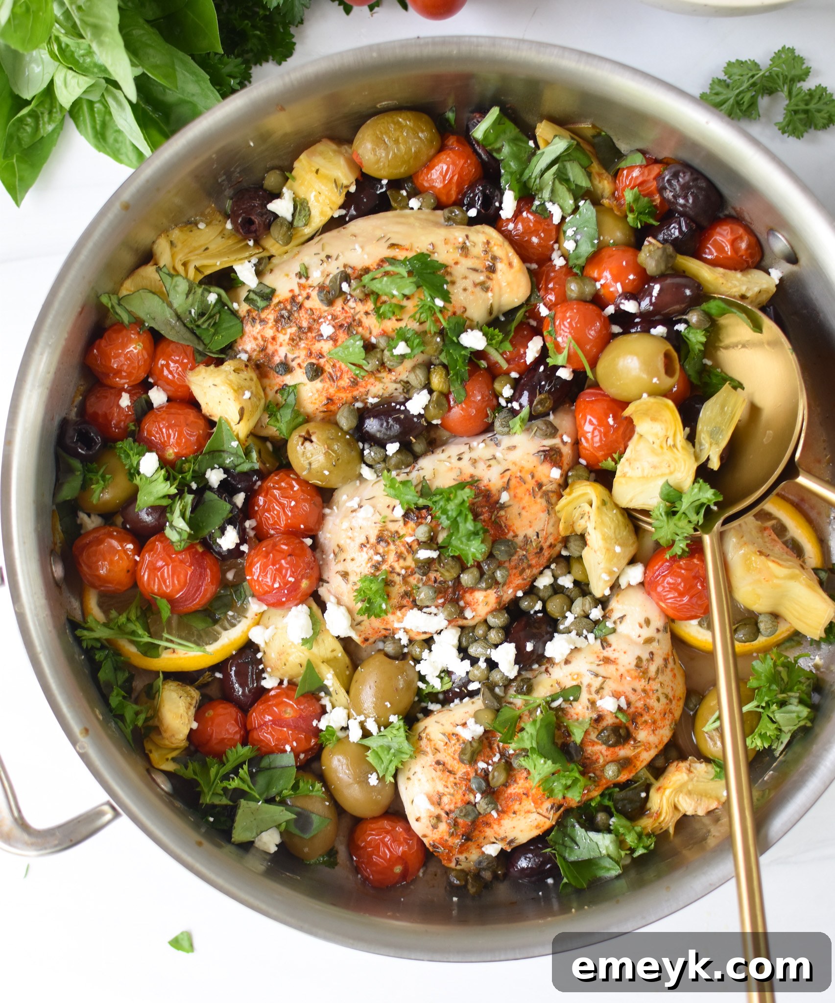 Mediterranean Skillet Chicken served directly in a rustic skillet with a fork and spoon, showcasing tender chicken pieces, bright cherry tomatoes, dark olives, and fresh herbs.