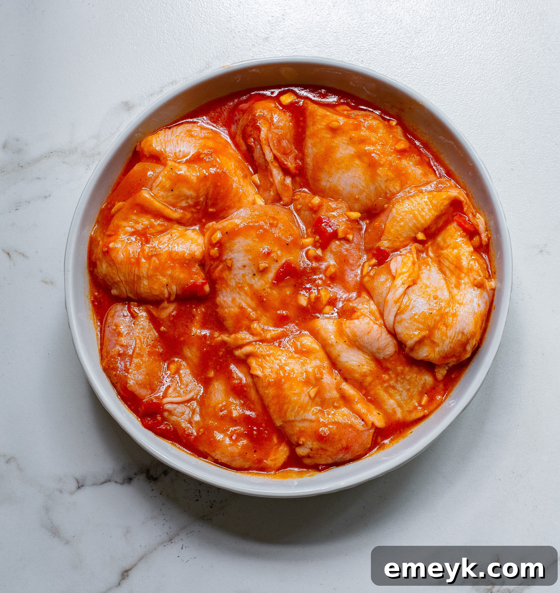 Chicken thighs coated with harissa marinade in a bowl.