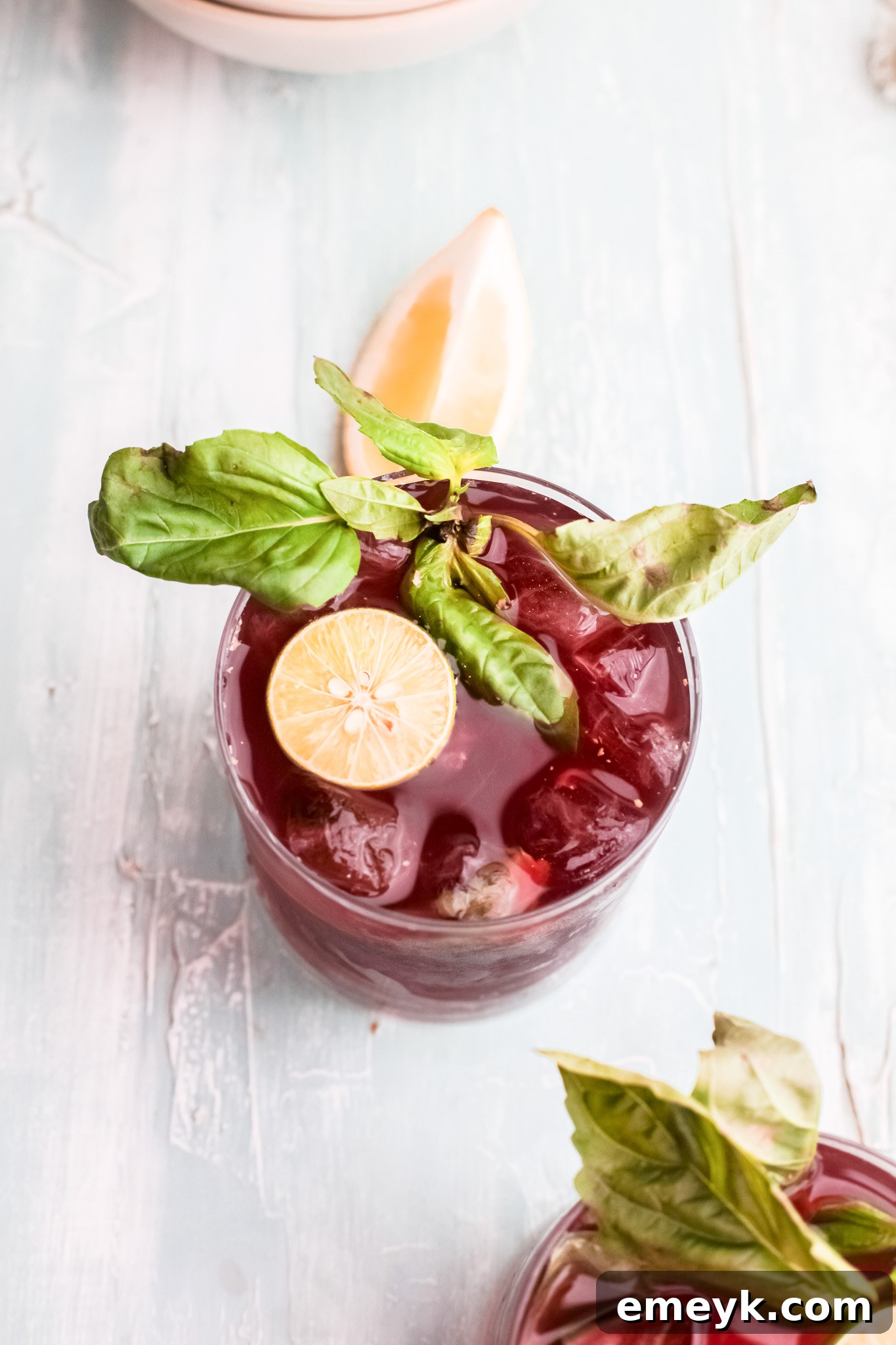 A close-up of Vodka Cherry Limeade garnished with lime and basil in a glass, with a refreshing look.