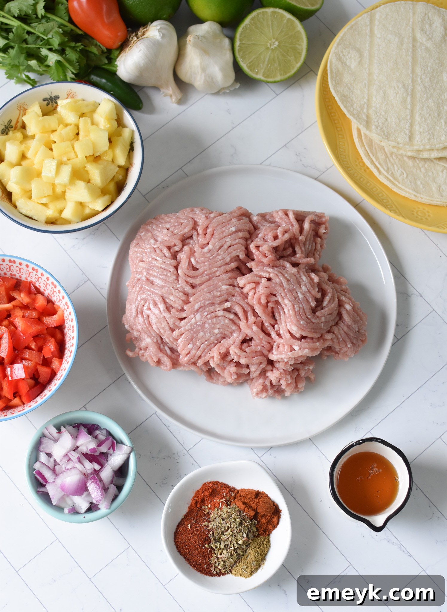 A collection of fresh ingredients for Easy Ground Pork Tacos, including ground pork, red onion, lime, honey, and spices, laid out on a clean surface.