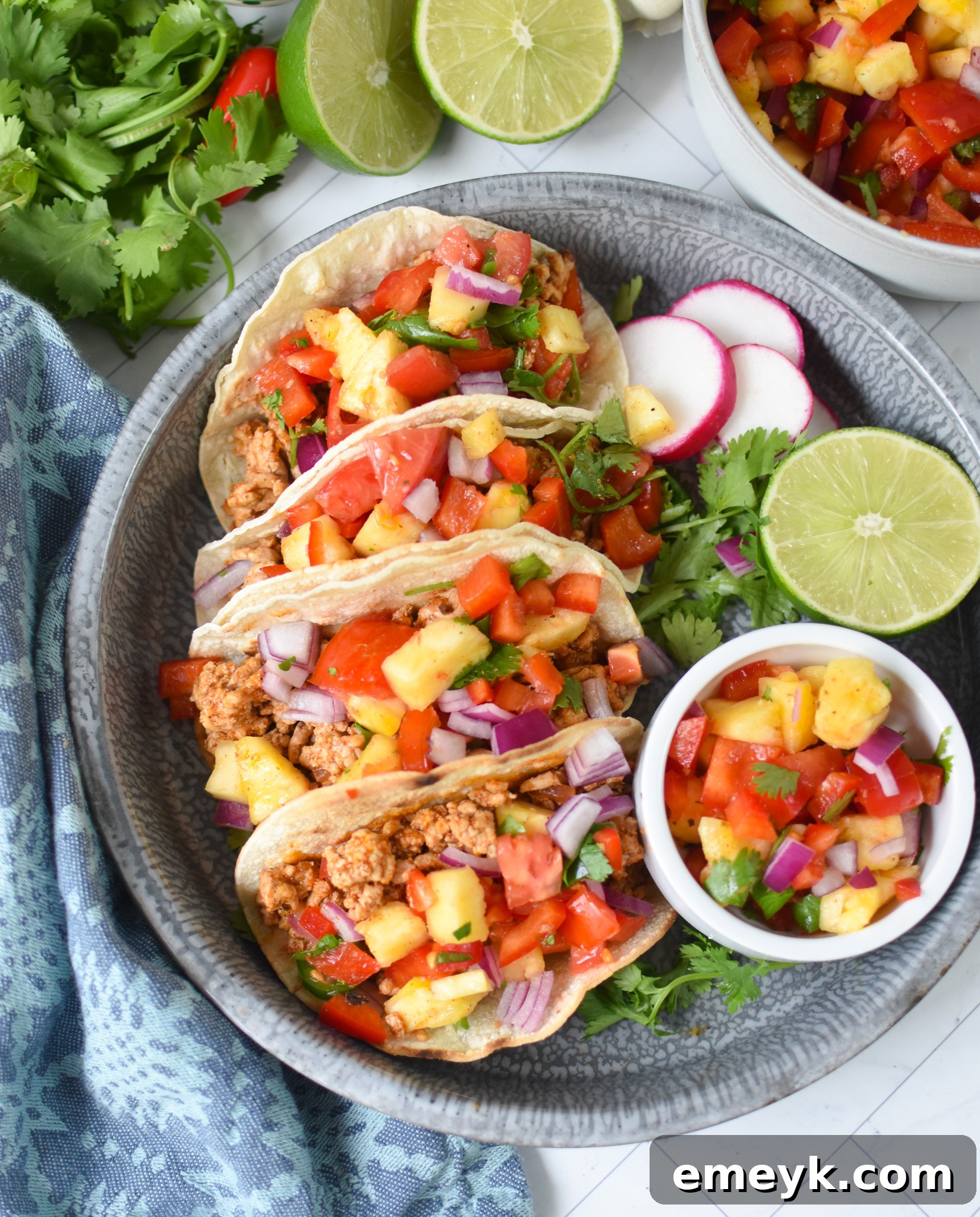 A vibrant platter of Easy Ground Pork Tacos, garnished with fresh cilantro, radish slices, and lime wedges, presented on a blue ceramic dish.