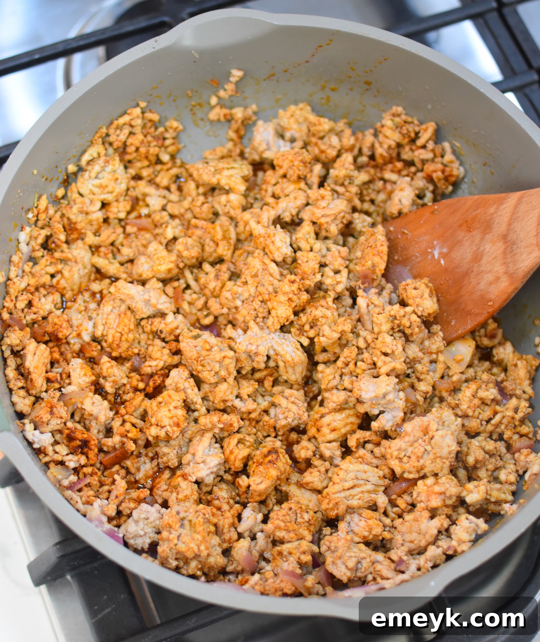 Close-up shot of seasoned ground pork cooking in a large skillet with onions and spices, ready for taco filling.
