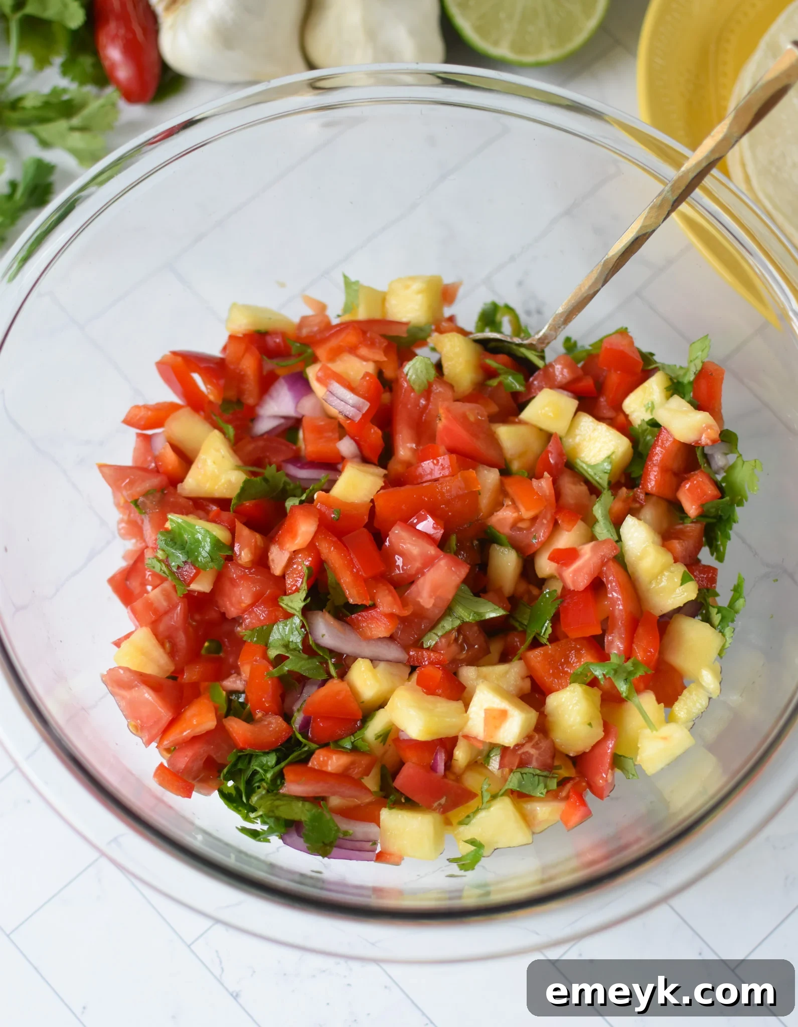 Freshly chopped ingredients for pineapple salsa, including pineapple chunks, red onion, bell pepper, tomatoes, cilantro, and jalapeños, in a large mixing bowl.