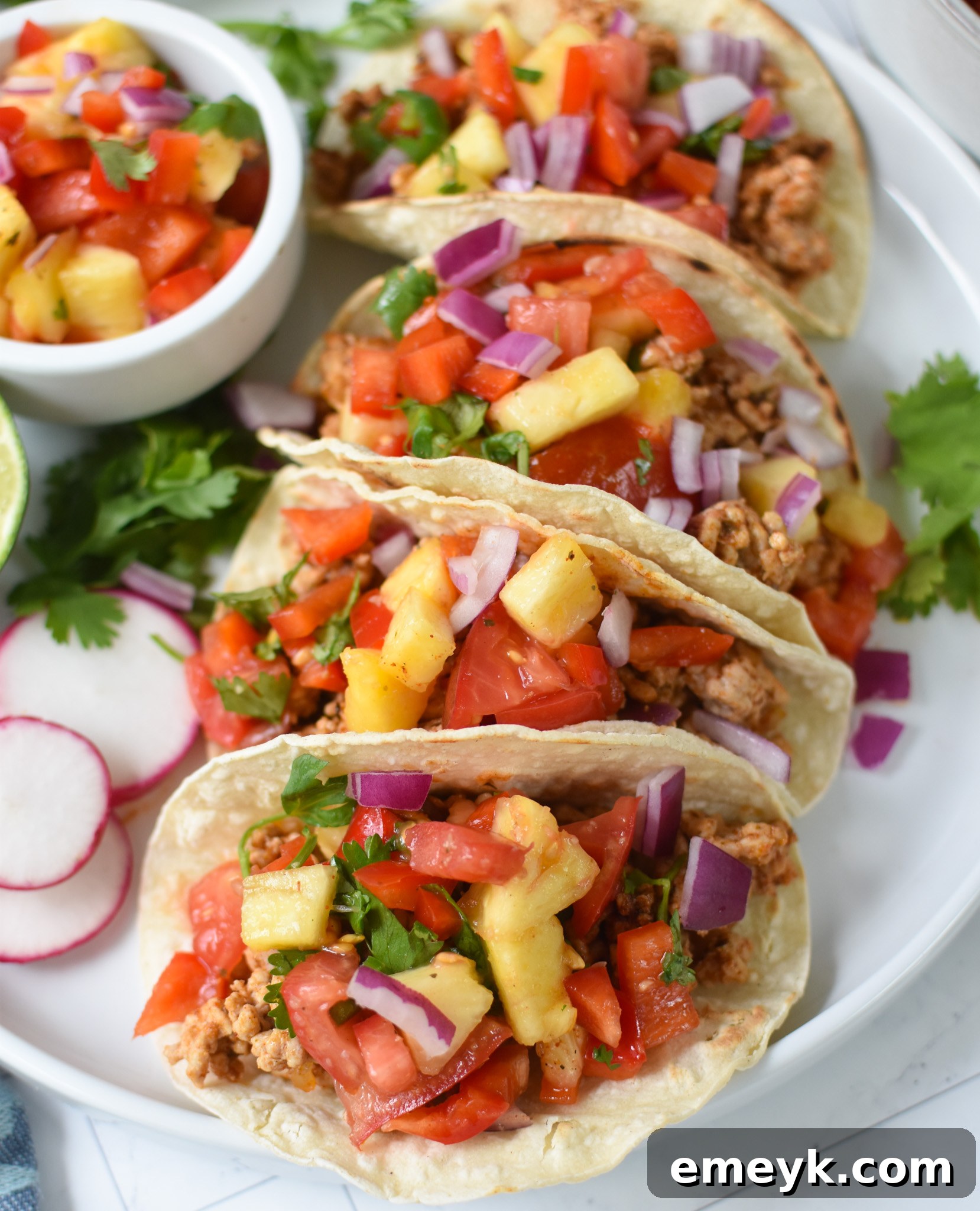 Two fully assembled Easy Ground Pork Tacos with a generous topping of pineapple salsa and fresh cilantro, displayed invitingly.