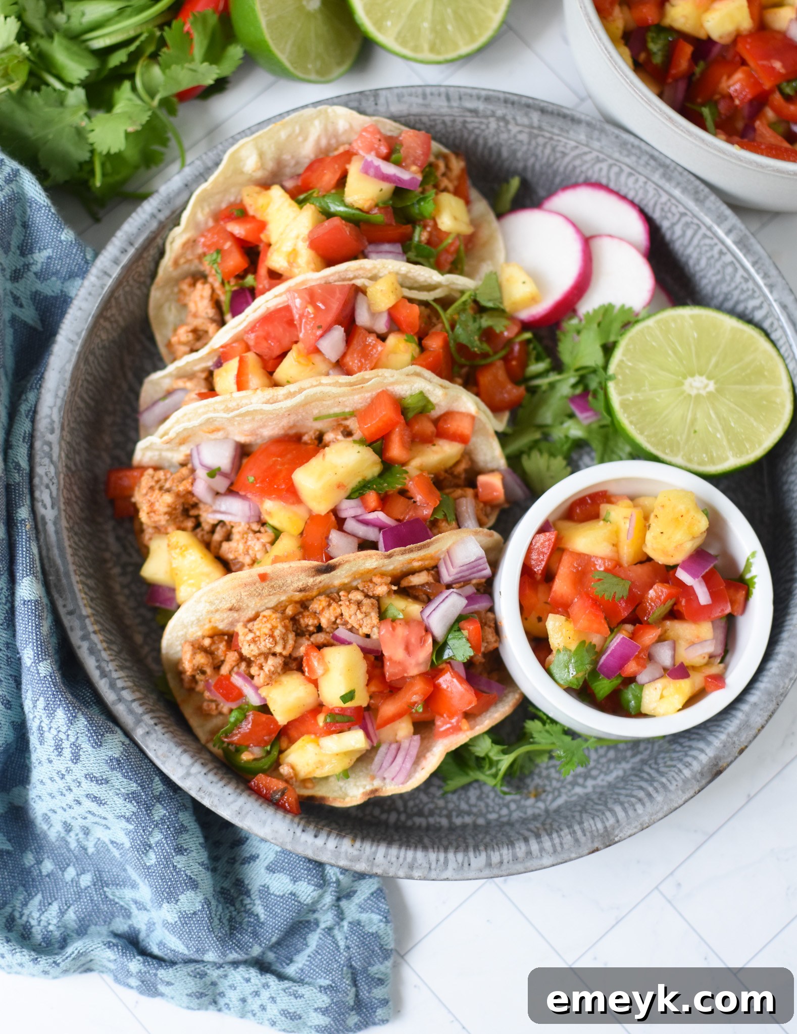 Easy Ground Pork Tacos garnished with fresh radishes, lime wedges, and cilantro, artfully arranged on a dark plate.