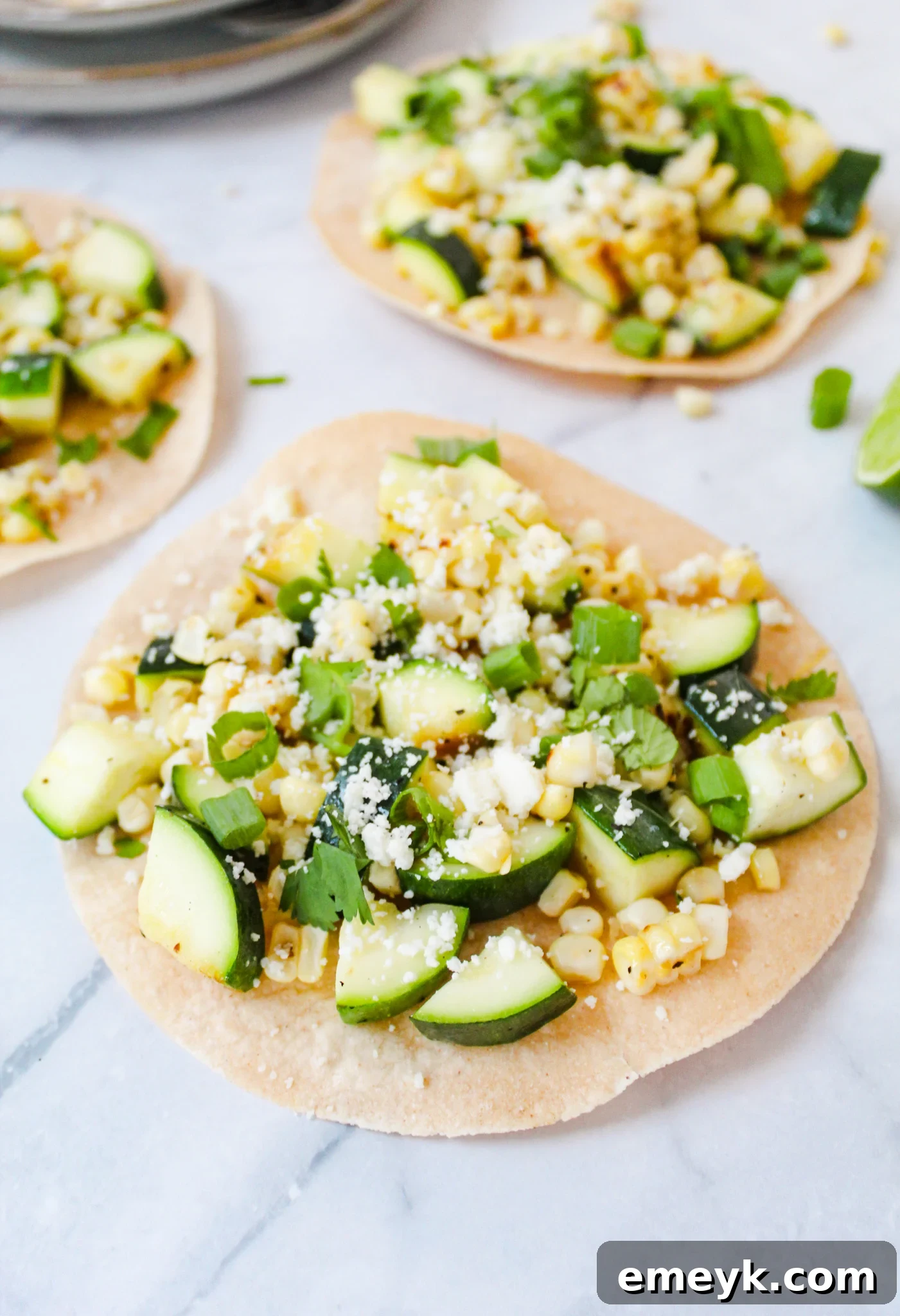 Platter of Easy Zucchini Tacos garnished with avocado, cilantro, and cotija cheese on a marble background