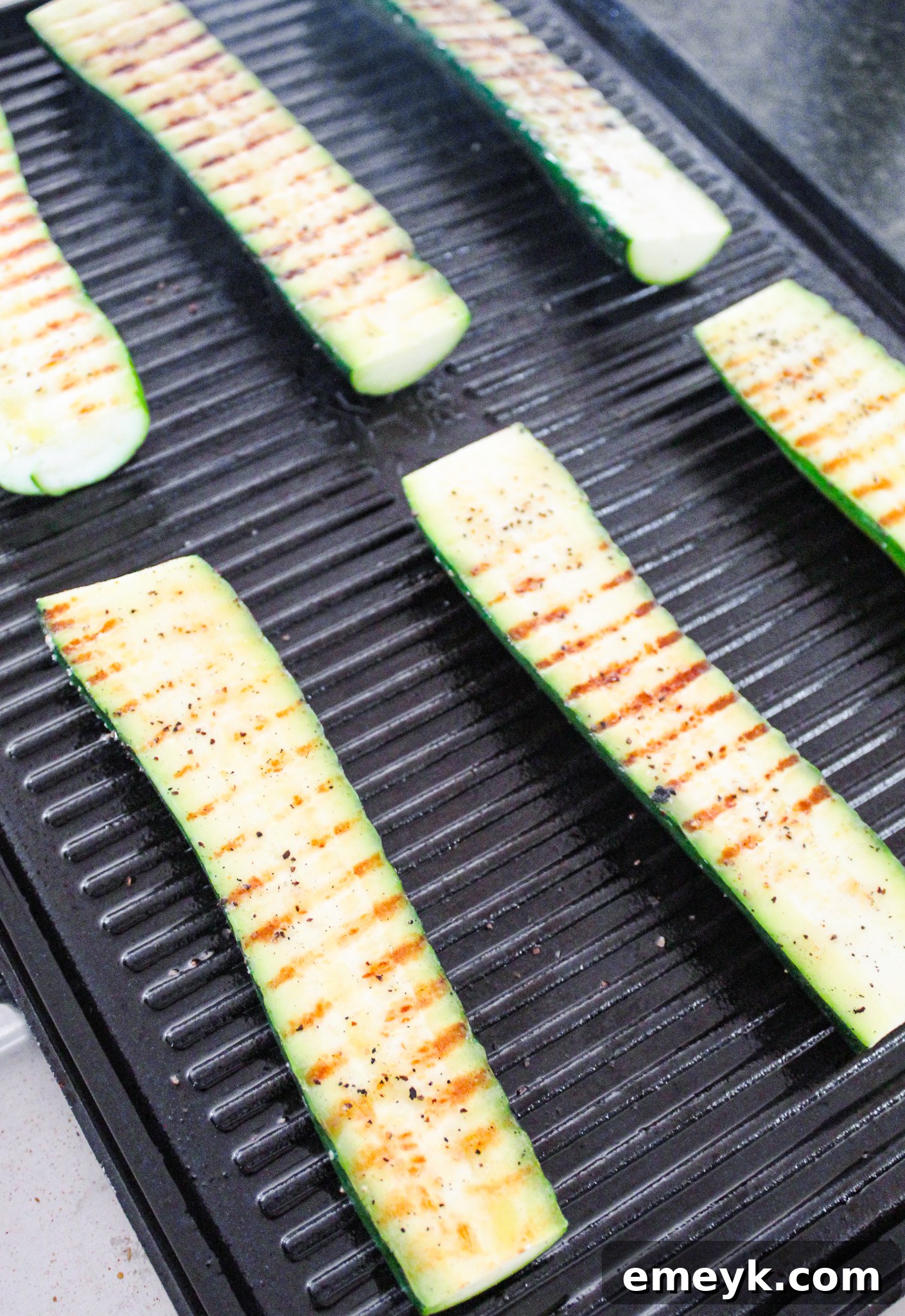 Zucchini halves grilling on a hot barbecue with visible char marks.