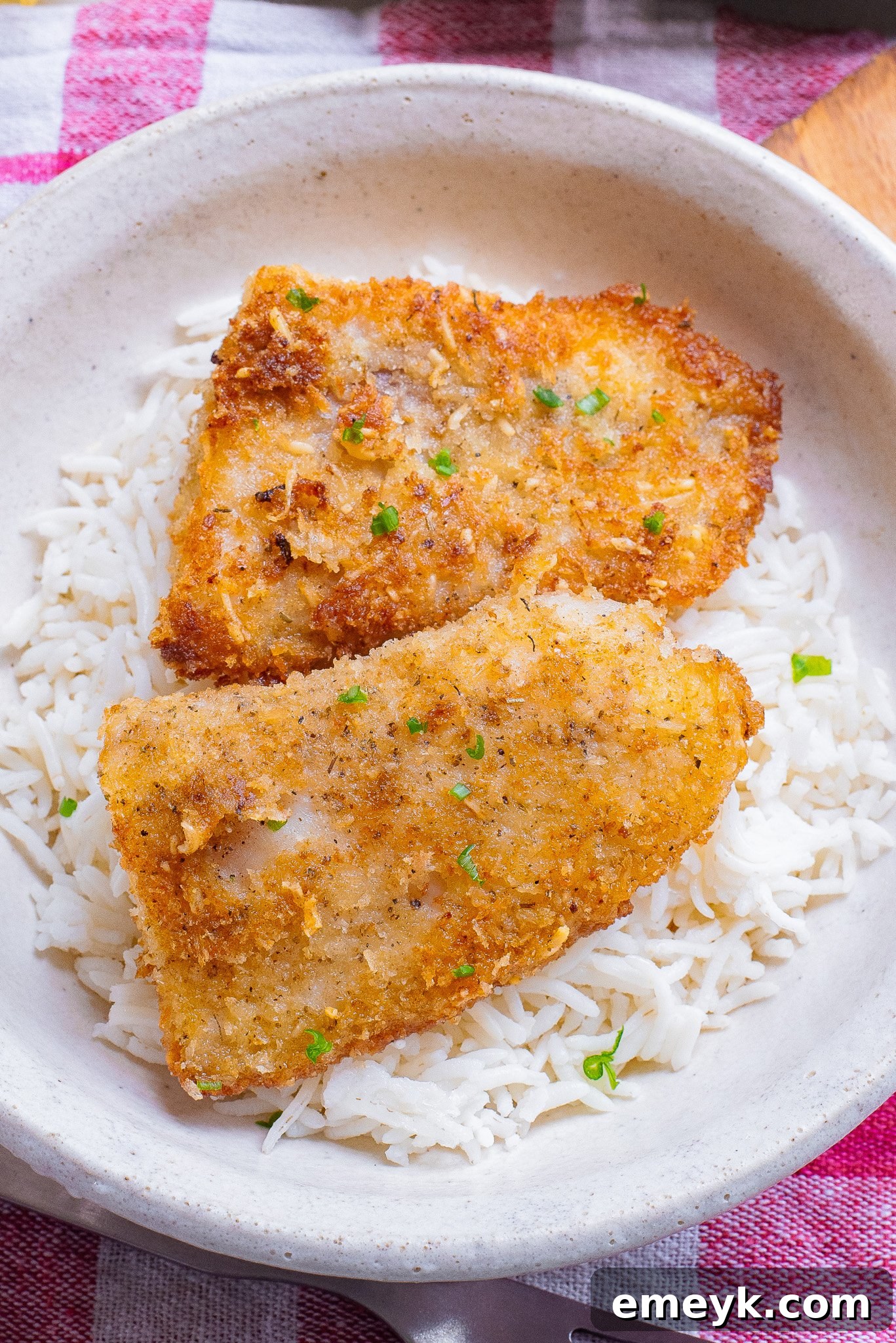 A serving of Easy Pan Fried Fish with a side of couscous and lemon wedges in a white bowl.