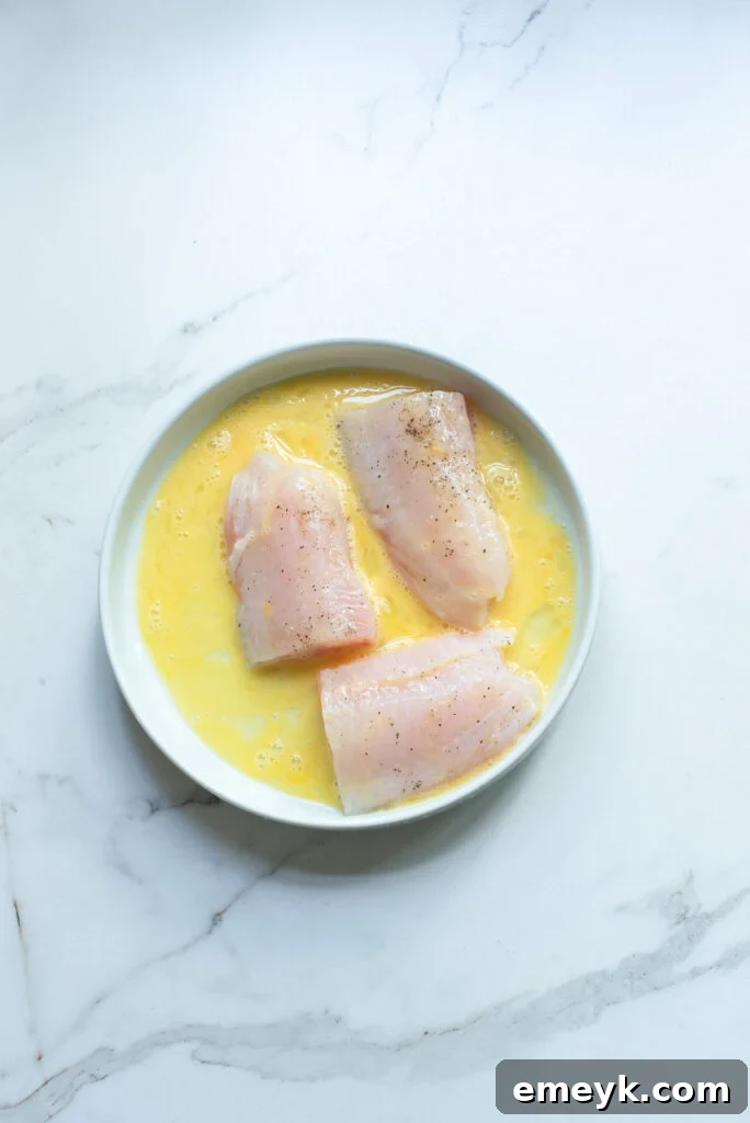 Fish fillet being dipped in beaten egg for pan frying.