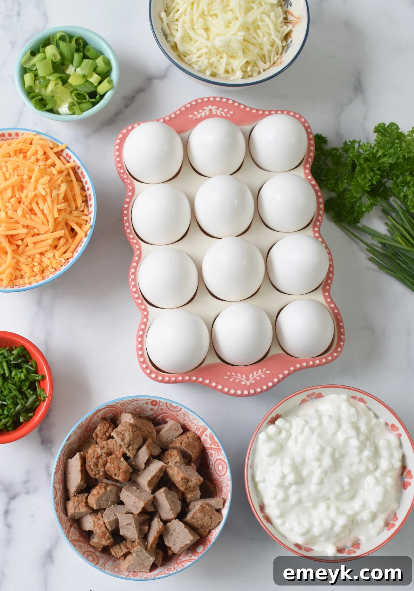 All the fresh and flavorful ingredients for Cheese and Sausage Baked Eggs laid out, including eggs, cheeses, spices, sausage, and herbs.