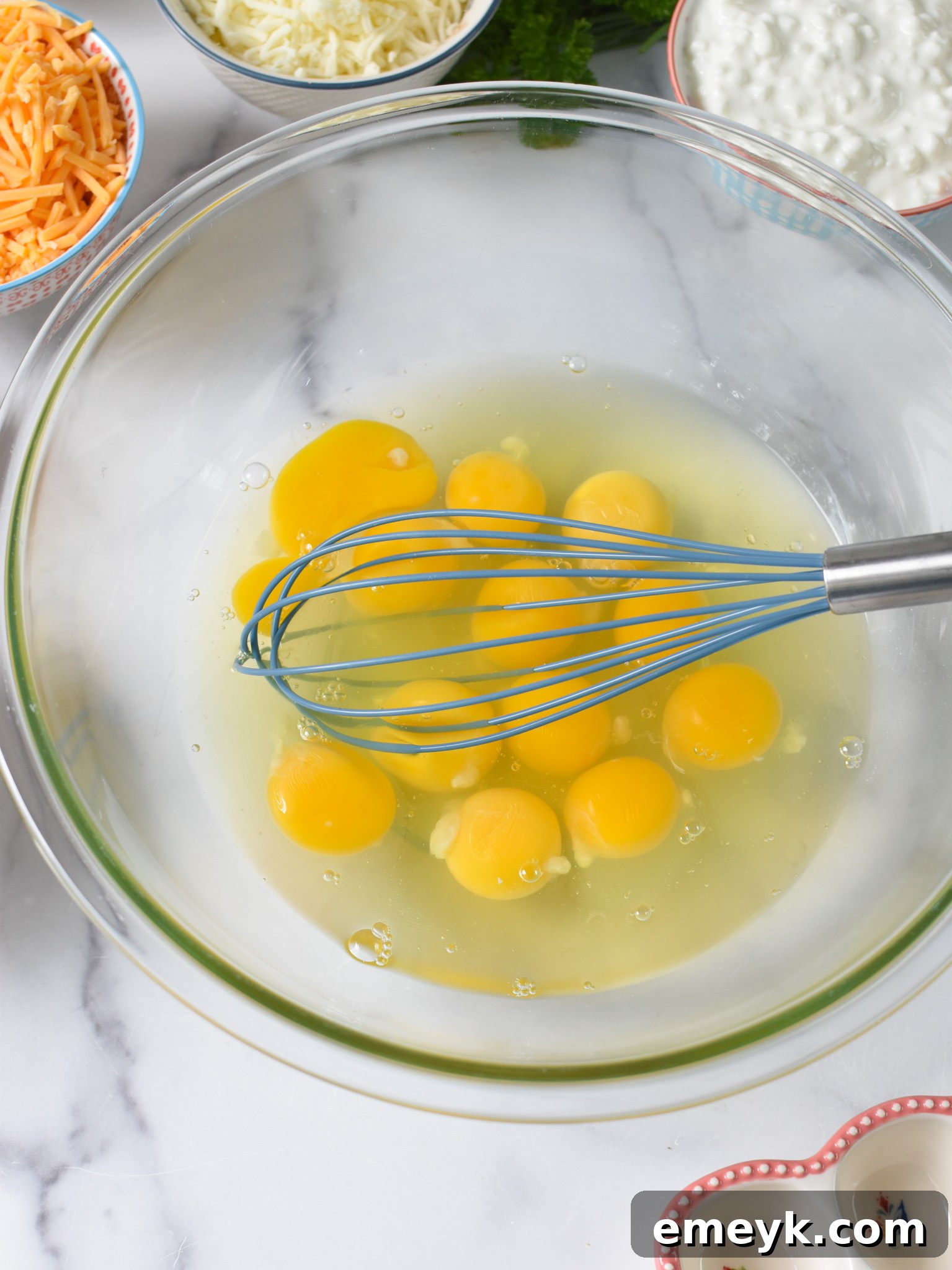 Close-up of eggs being whisked in a glass bowl, a crucial first step for the Cheese and Sausage Baked Eggs.