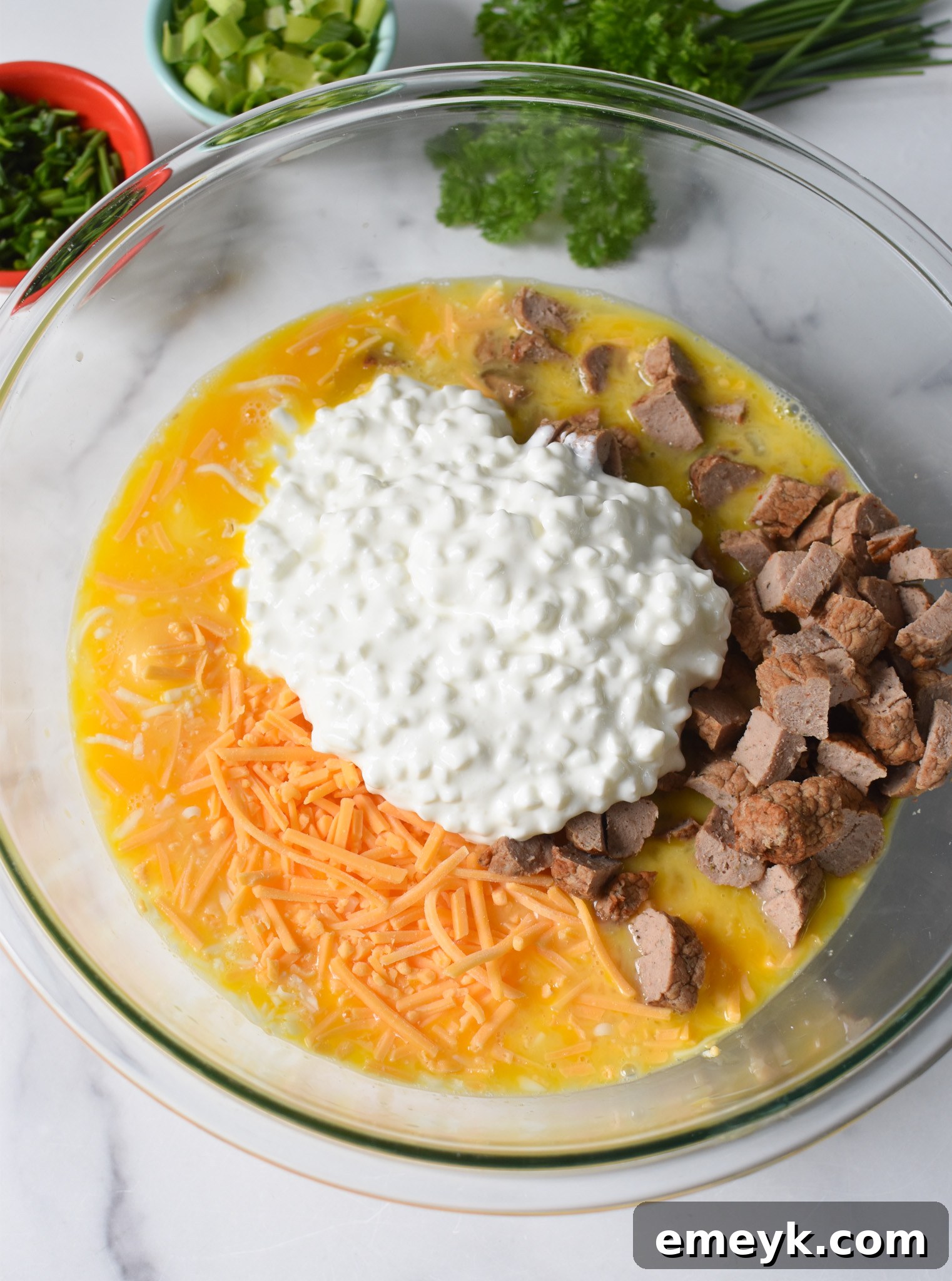 All the ingredients for Cheese and Sausage Baked Eggs, including eggs, cheeses, and spices, mixed together in a large mixing bowl.
