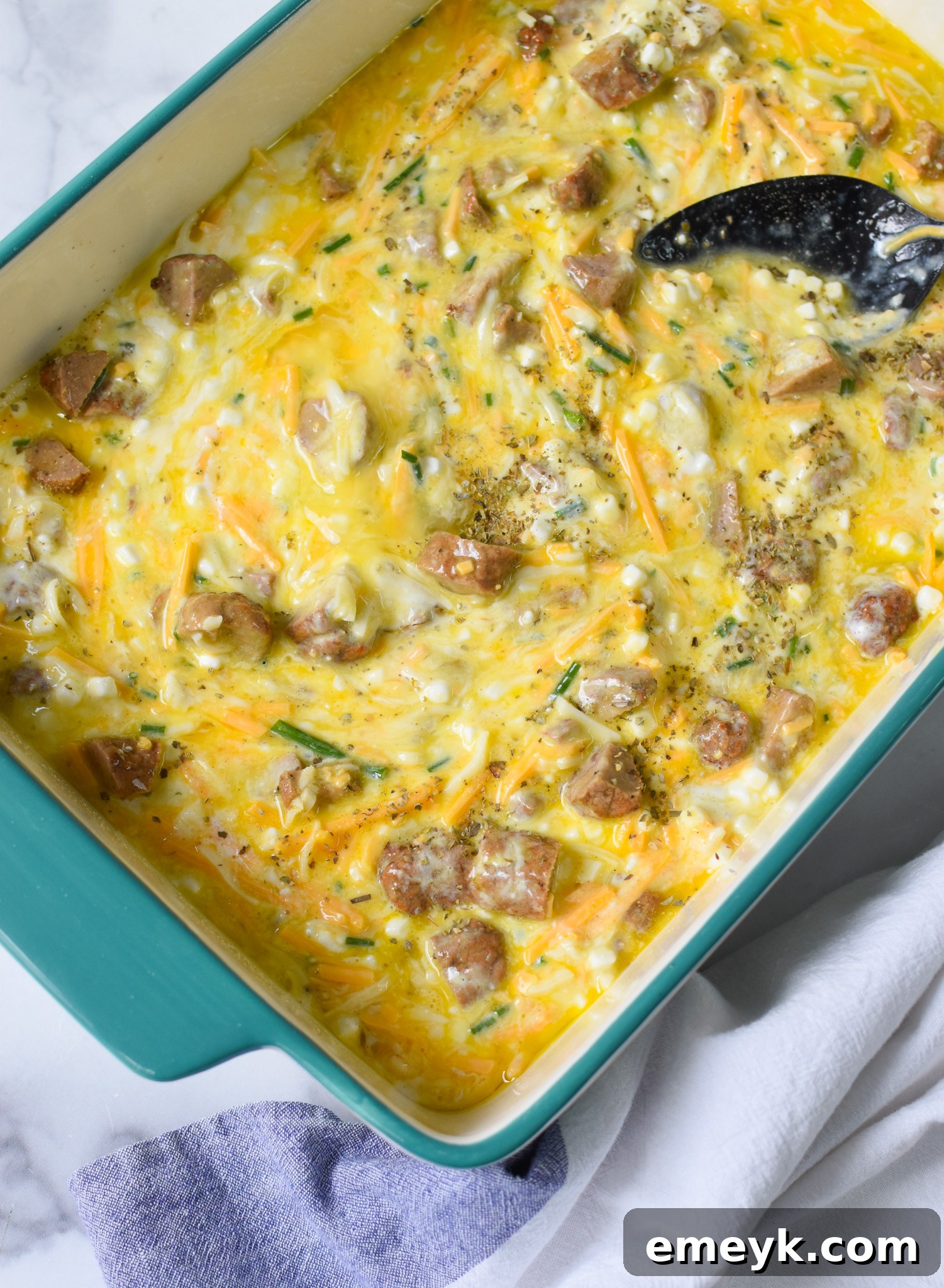The mixed Cheese and Sausage Baked Eggs ingredients poured into a casserole dish, ready for the oven.