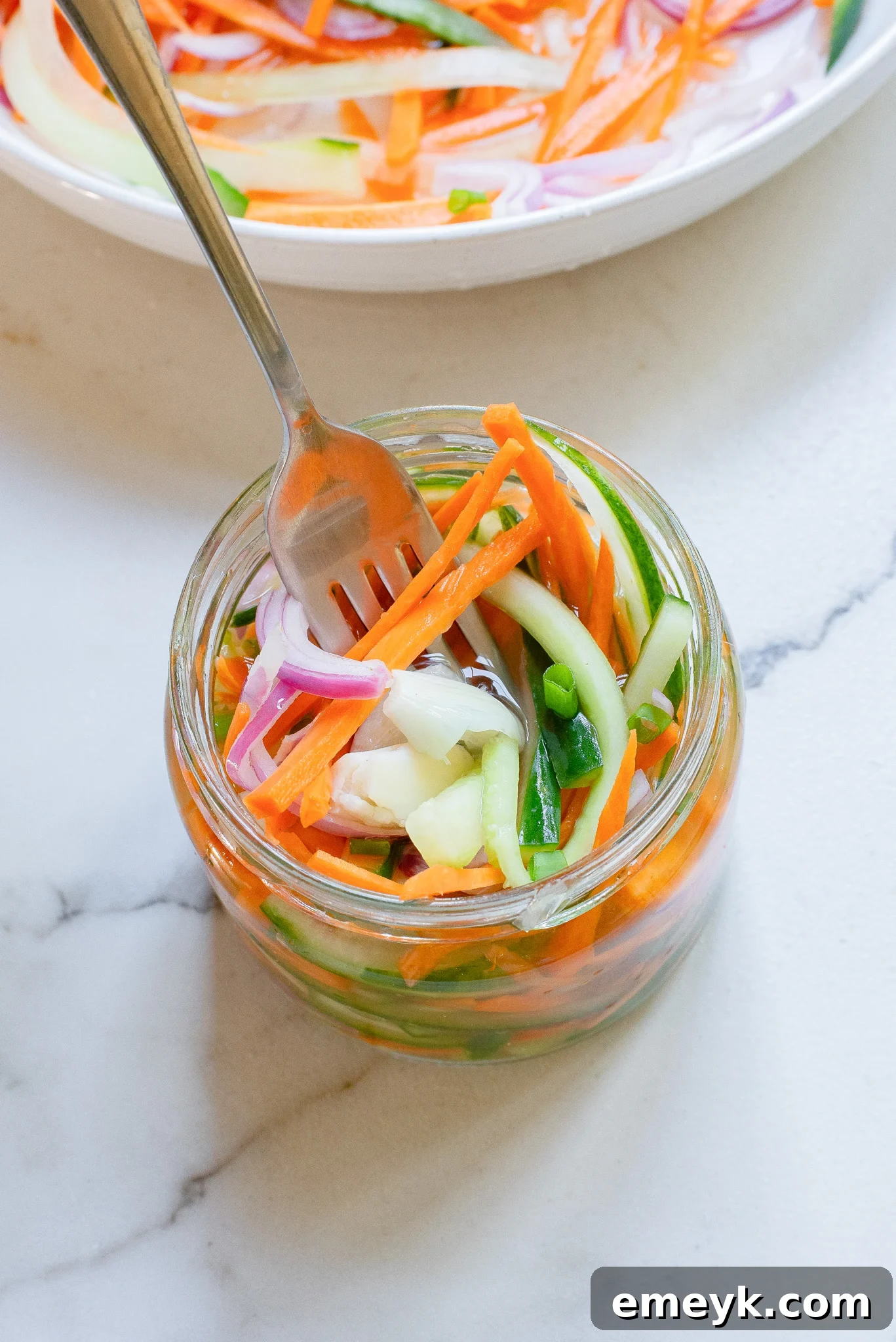 A mason jar filled with colorful quick pickled vegetables, with a fork reaching in for a bite.