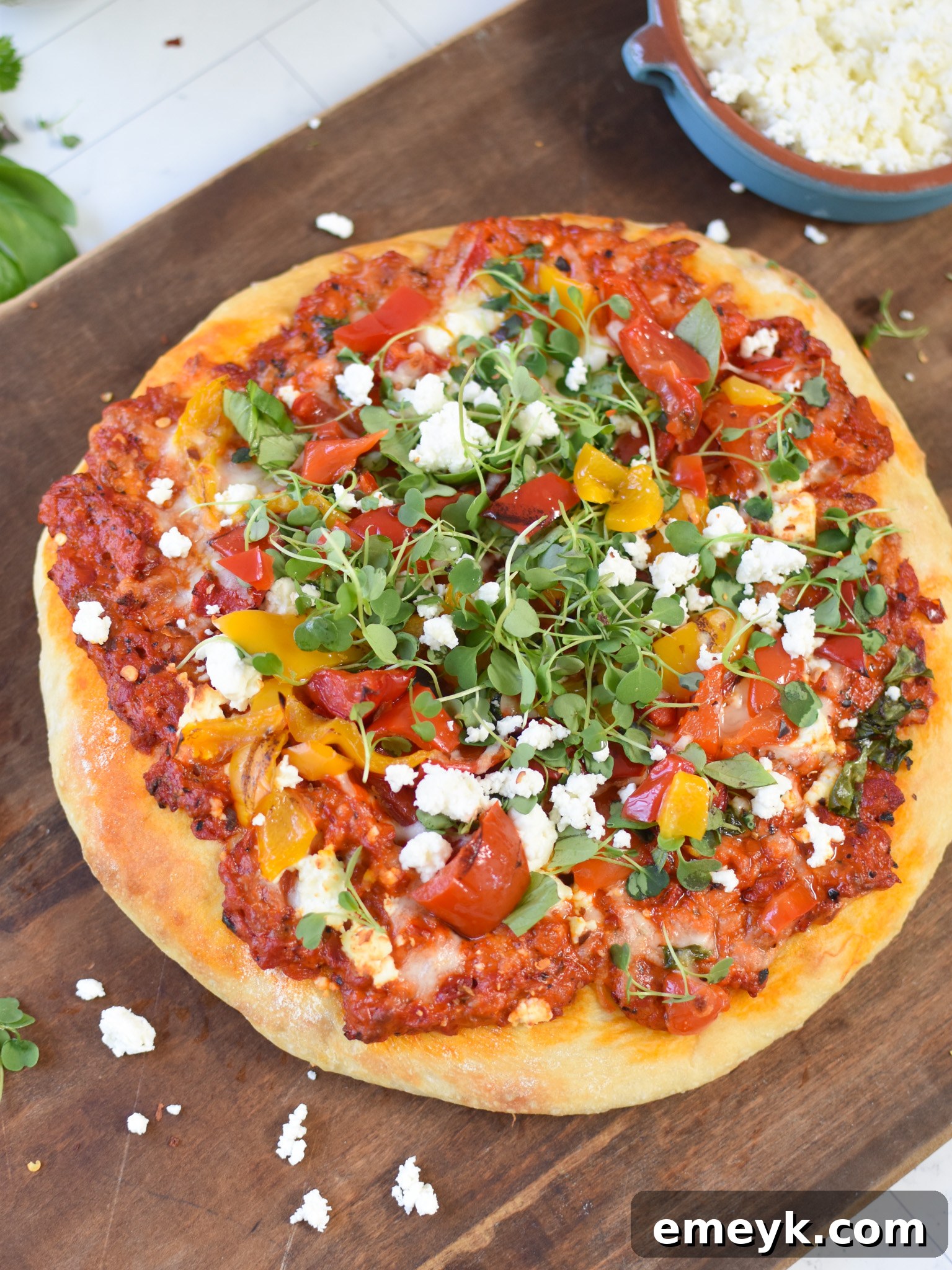 A beautifully garnished Cast Iron Mediterranean Pizza on a wooden cutting board, ready for slicing.
