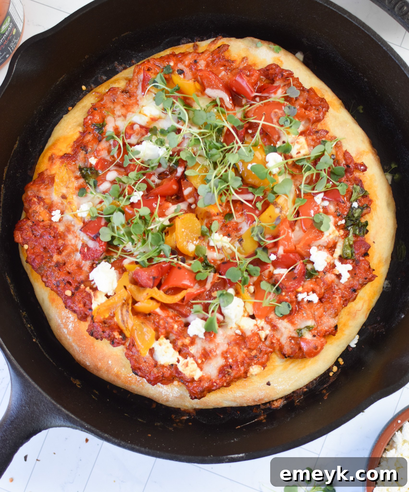 A whole Cast Iron Mediterranean Pizza, still hot in its skillet, showing off its golden crust and melted toppings.