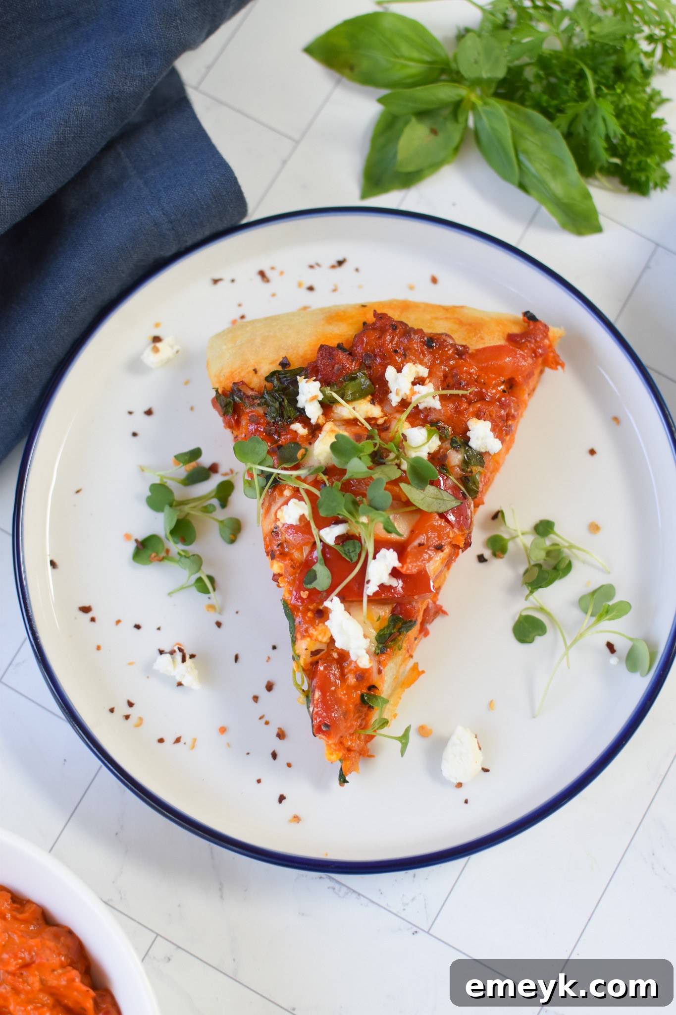 A visually appealing slice of Cast Iron Mediterranean Pizza resting on a crisp white plate, elegantly garnished with fresh microgreens, highlighting its vibrant colors and inviting textures.
