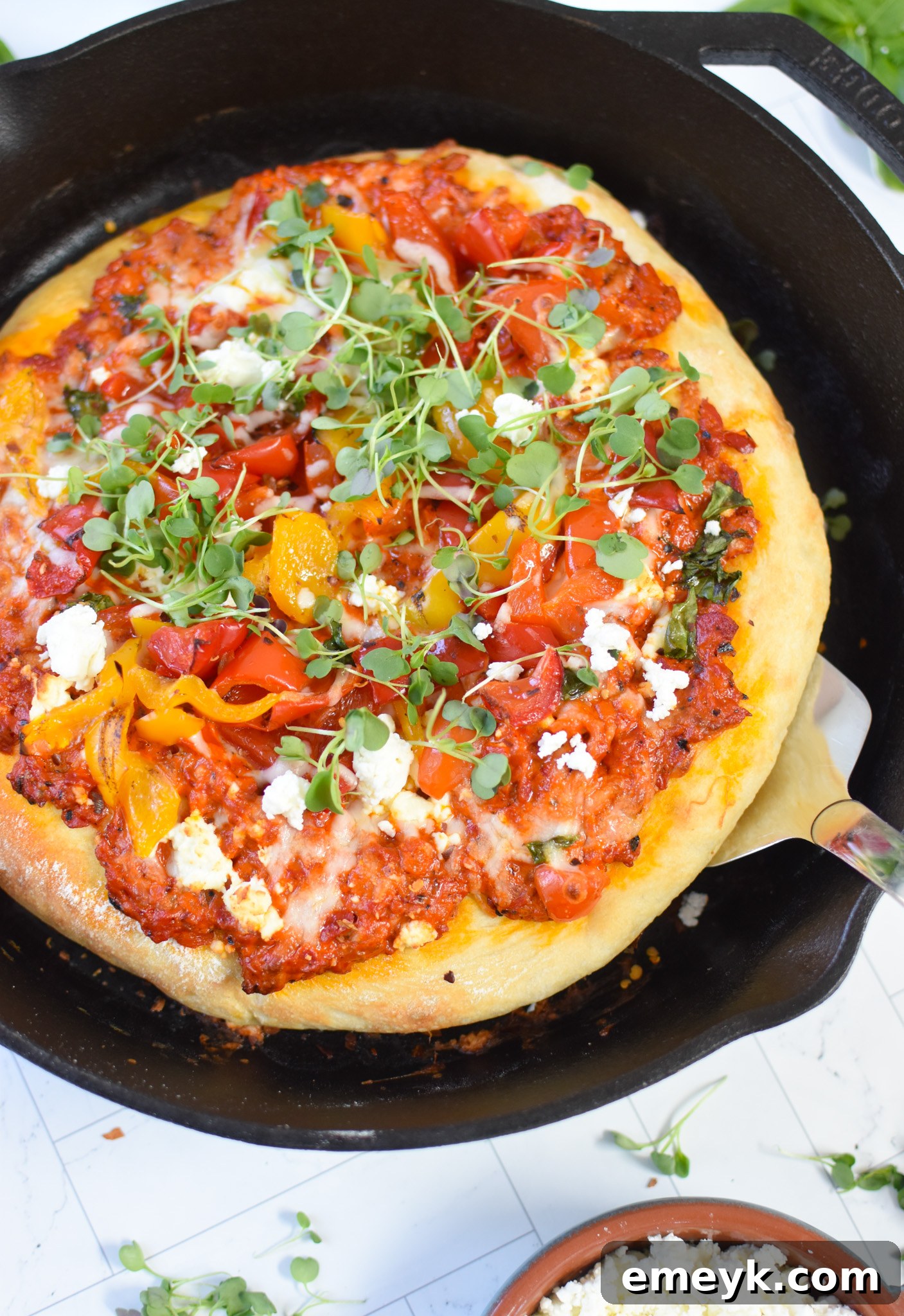 A Cast Iron Mediterranean Pizza in the skillet with a spatula poised to lift a slice, symbolizing perfect readiness for serving.