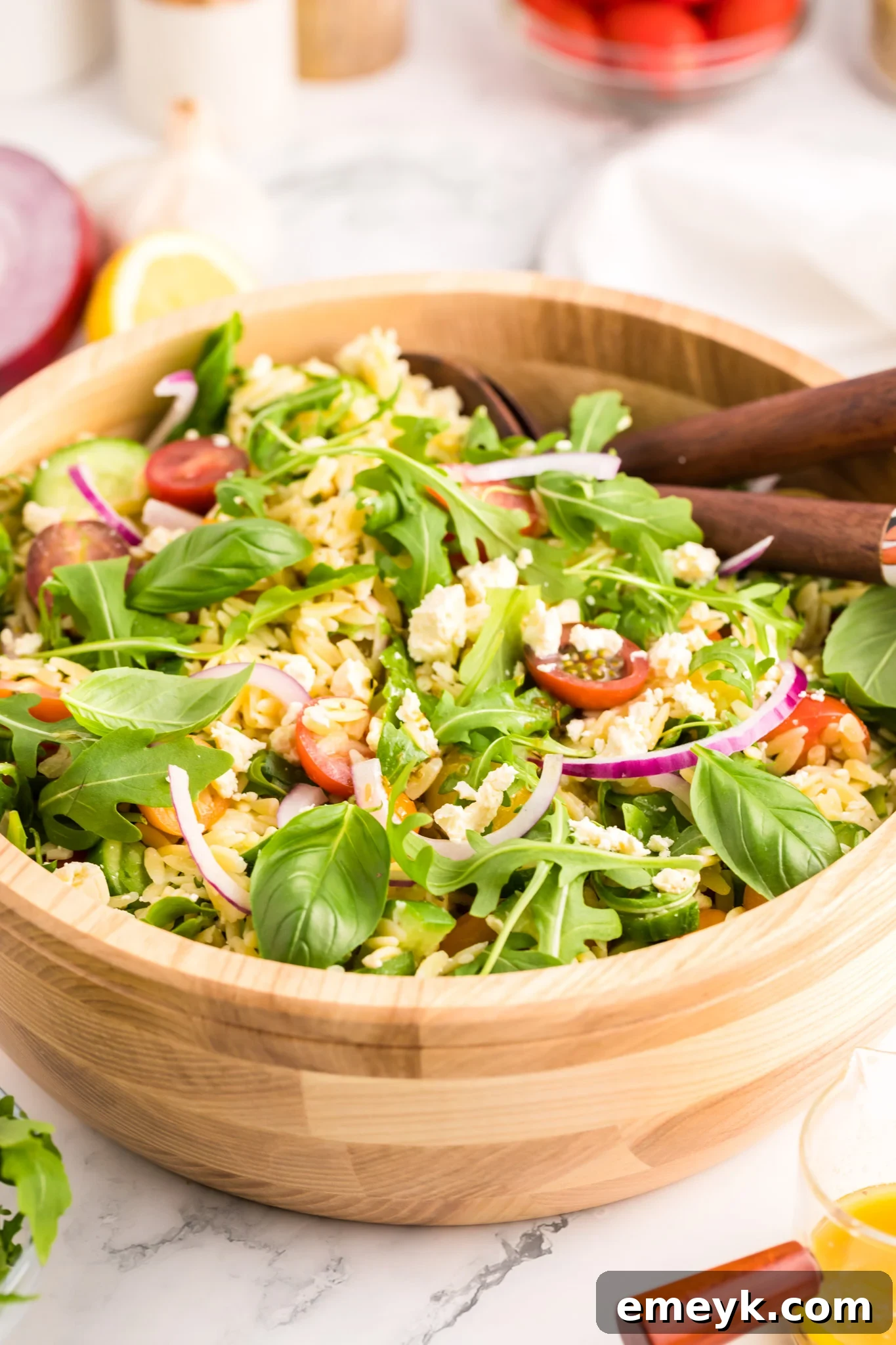 A vibrant Arugula Orzo Salad served in a bowl with wooden spoons, highlighting fresh ingredients.